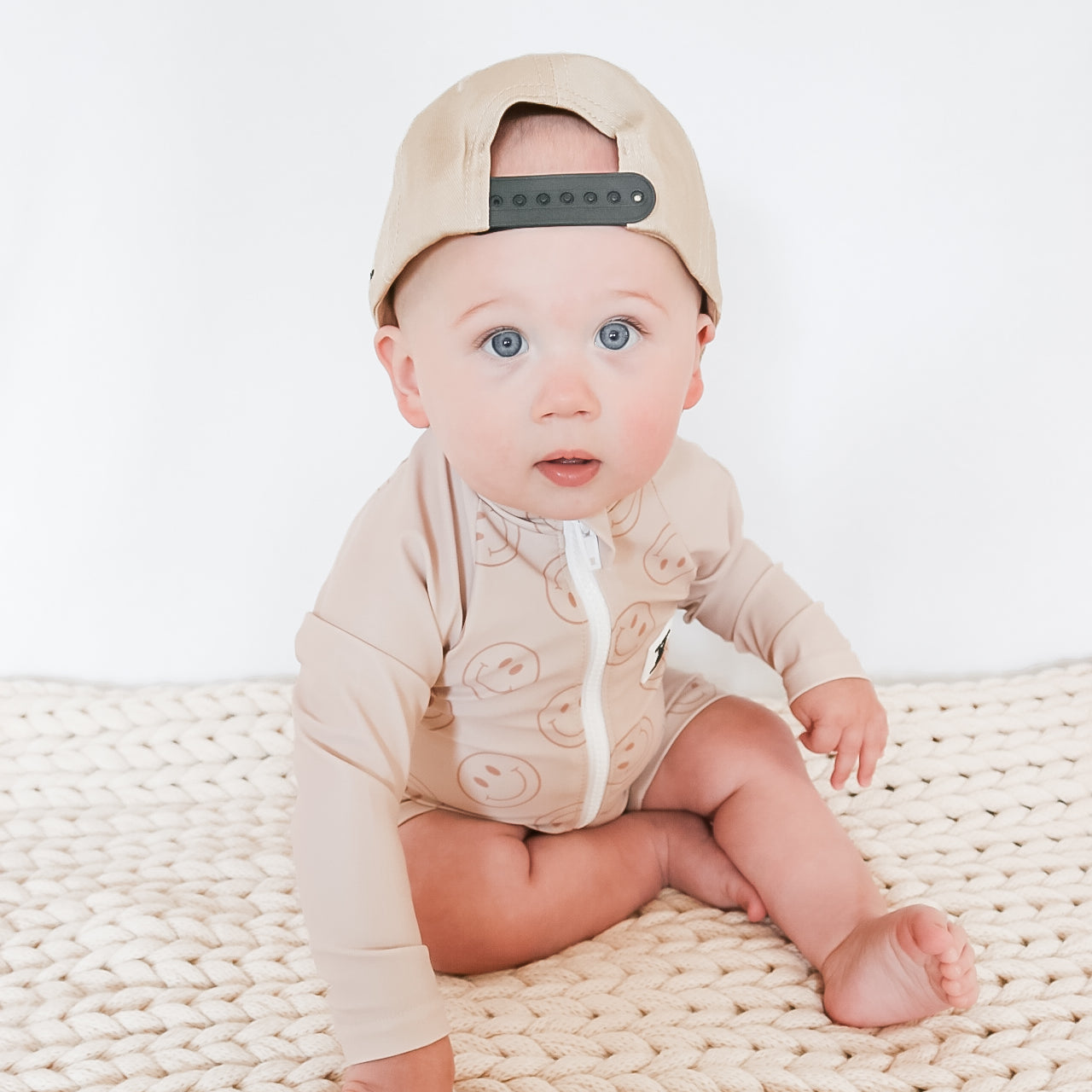 cute boy wearing Rad Toddlers Smiley Shore One-Piece Rashguard in beige with smiley face design, featuring easy zipper and UPF 50+ sun protection.