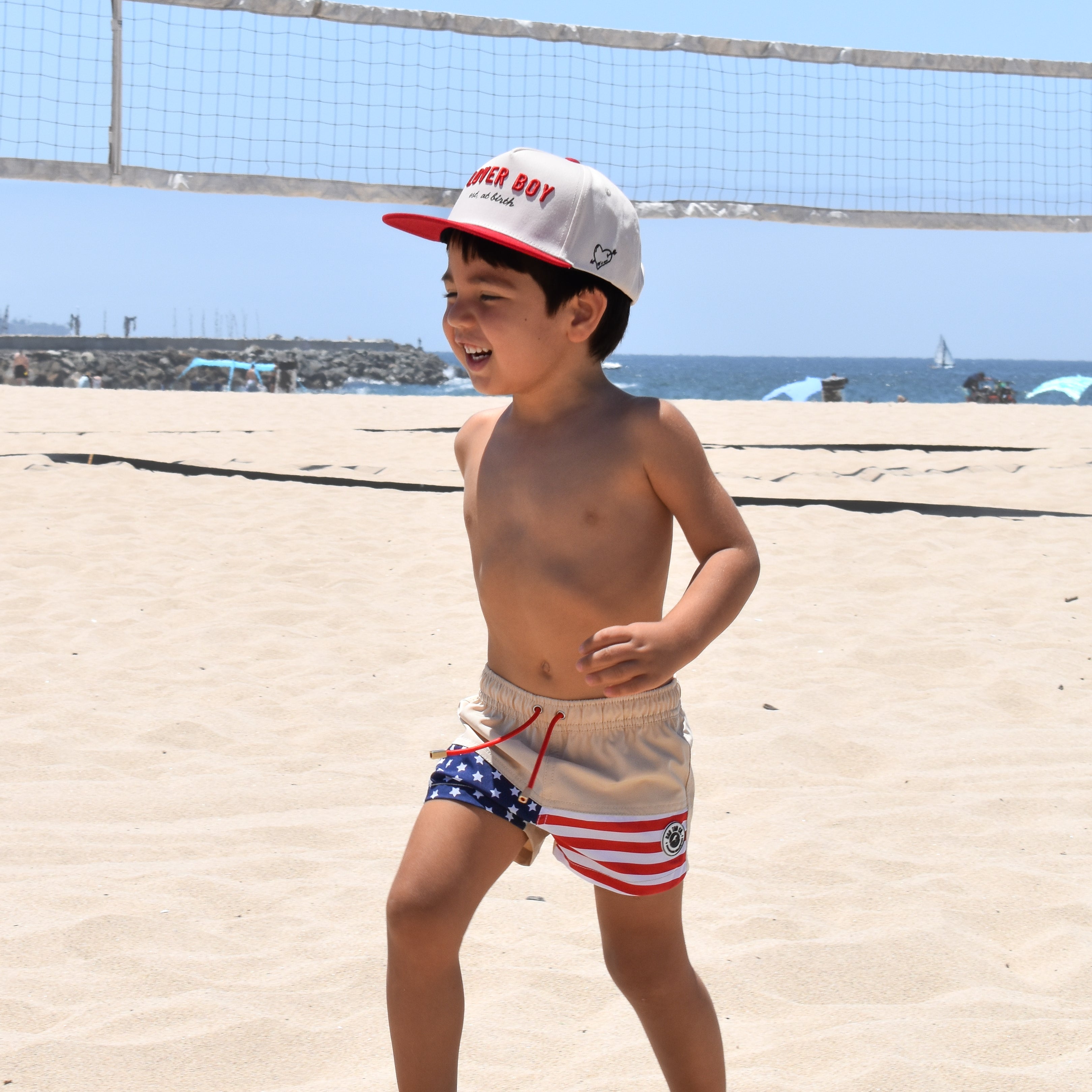 Child in swim trunks and cap on a sandy beach with ocean view