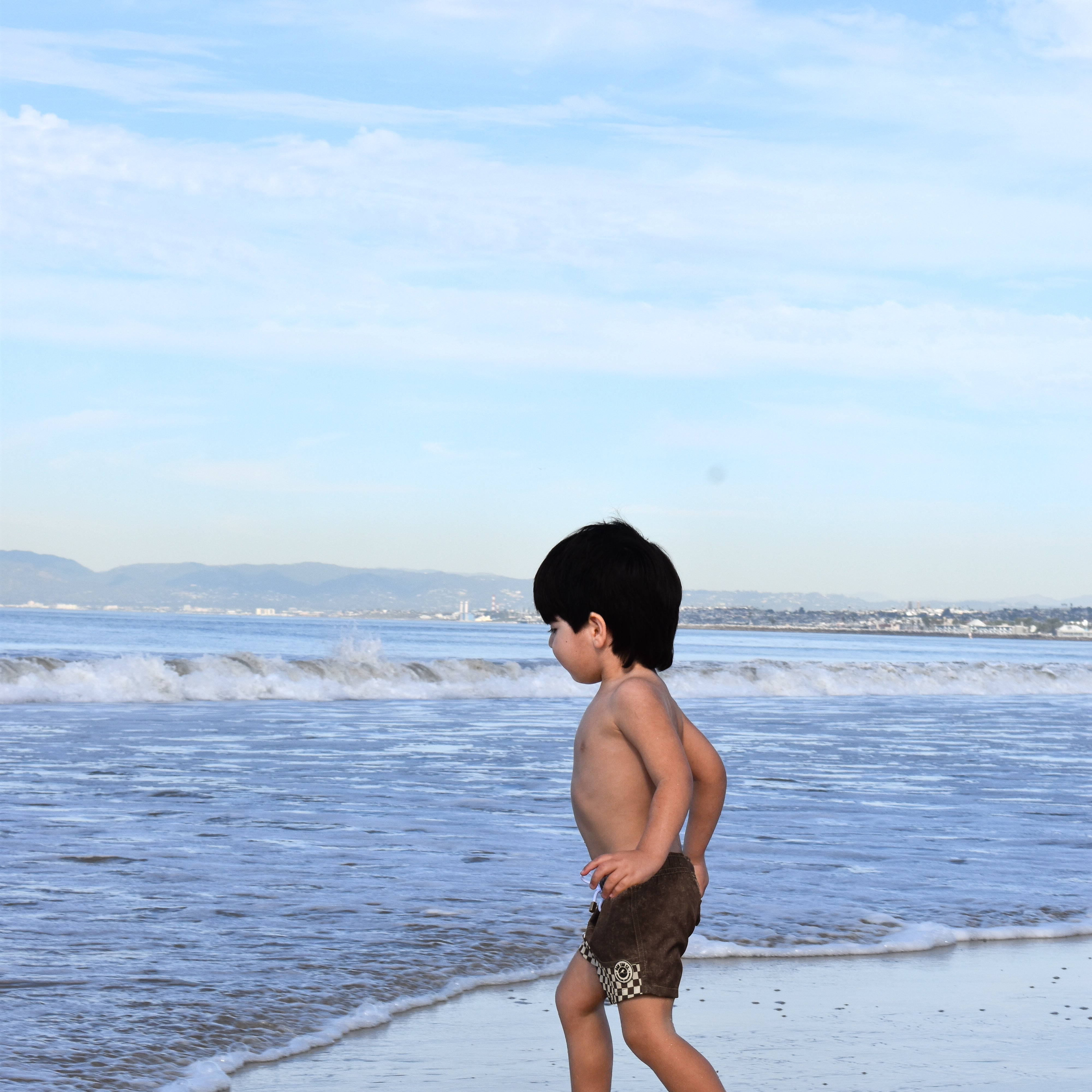 Child walking on a beach with clear blue sky and ocean waves.