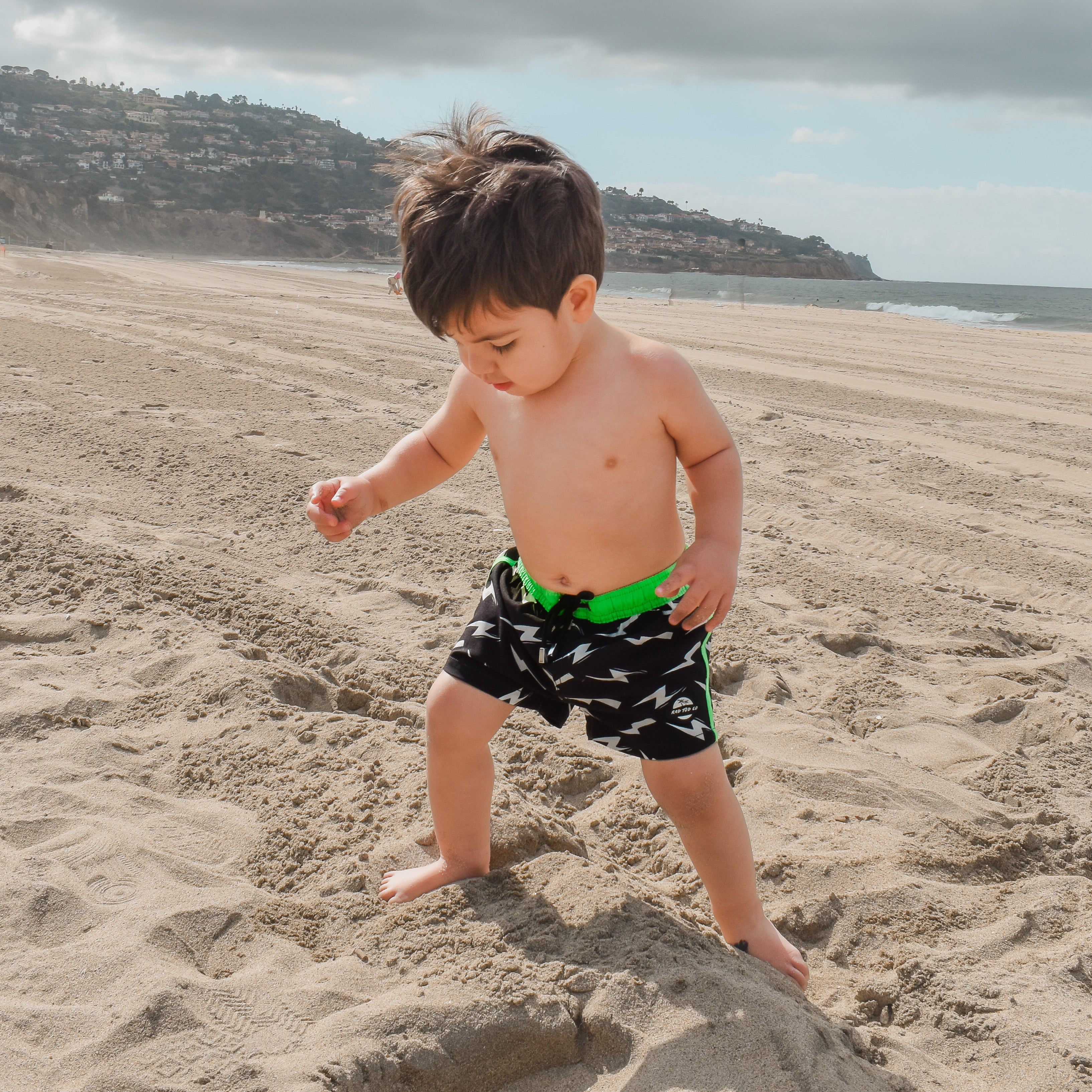 adventurous boy wearing Bright swim shorts with an elastic waistband and drawstring, made from quick-drying fabric. Ideal for swimming, beach trips, and outdoor activities. Features vibrant patterns and a comfortable fit for active kids.