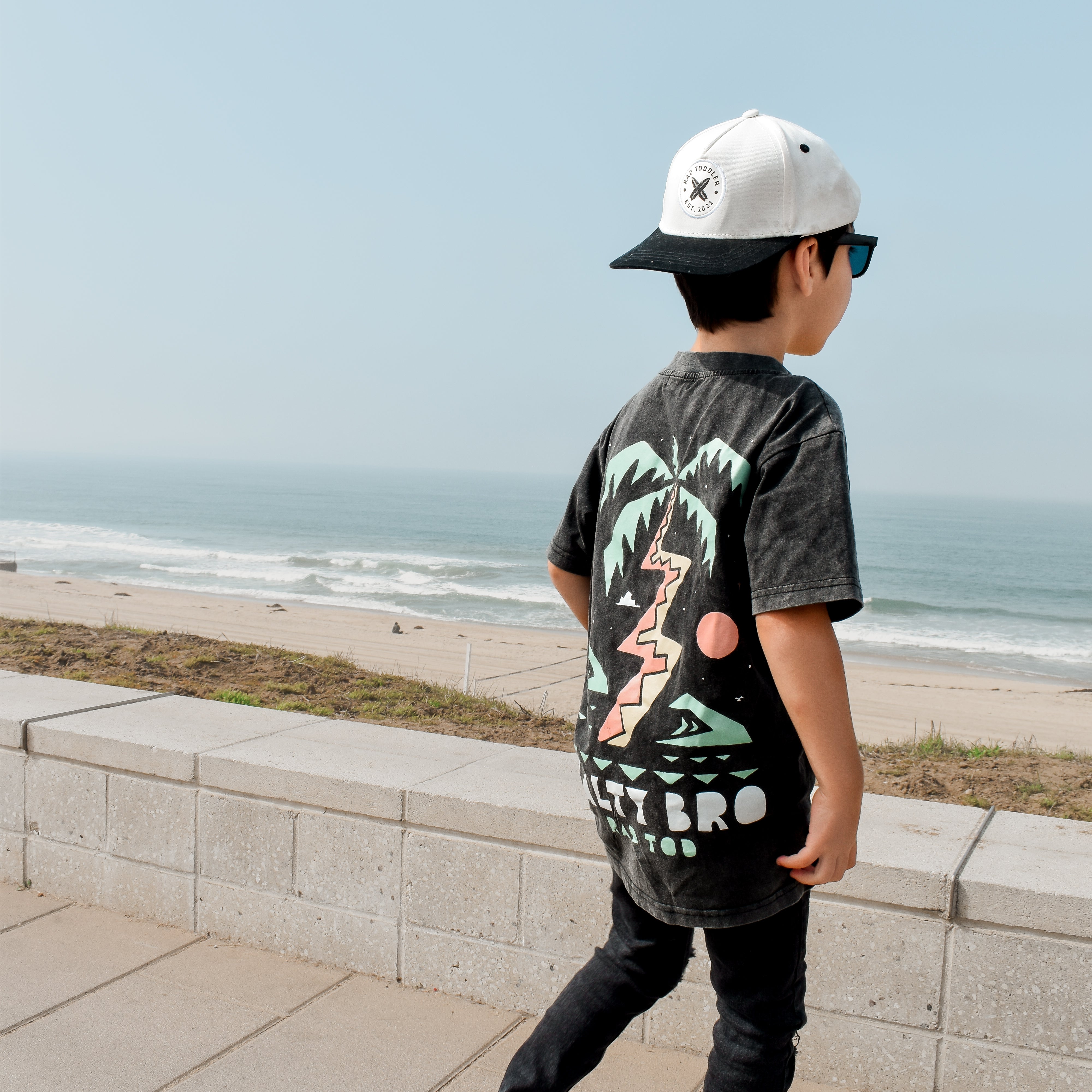 boy checking out the beach wearing Rad Toddler black acid wash toddler tee with bold 'Salty Bro' text in playful, beach style lettering