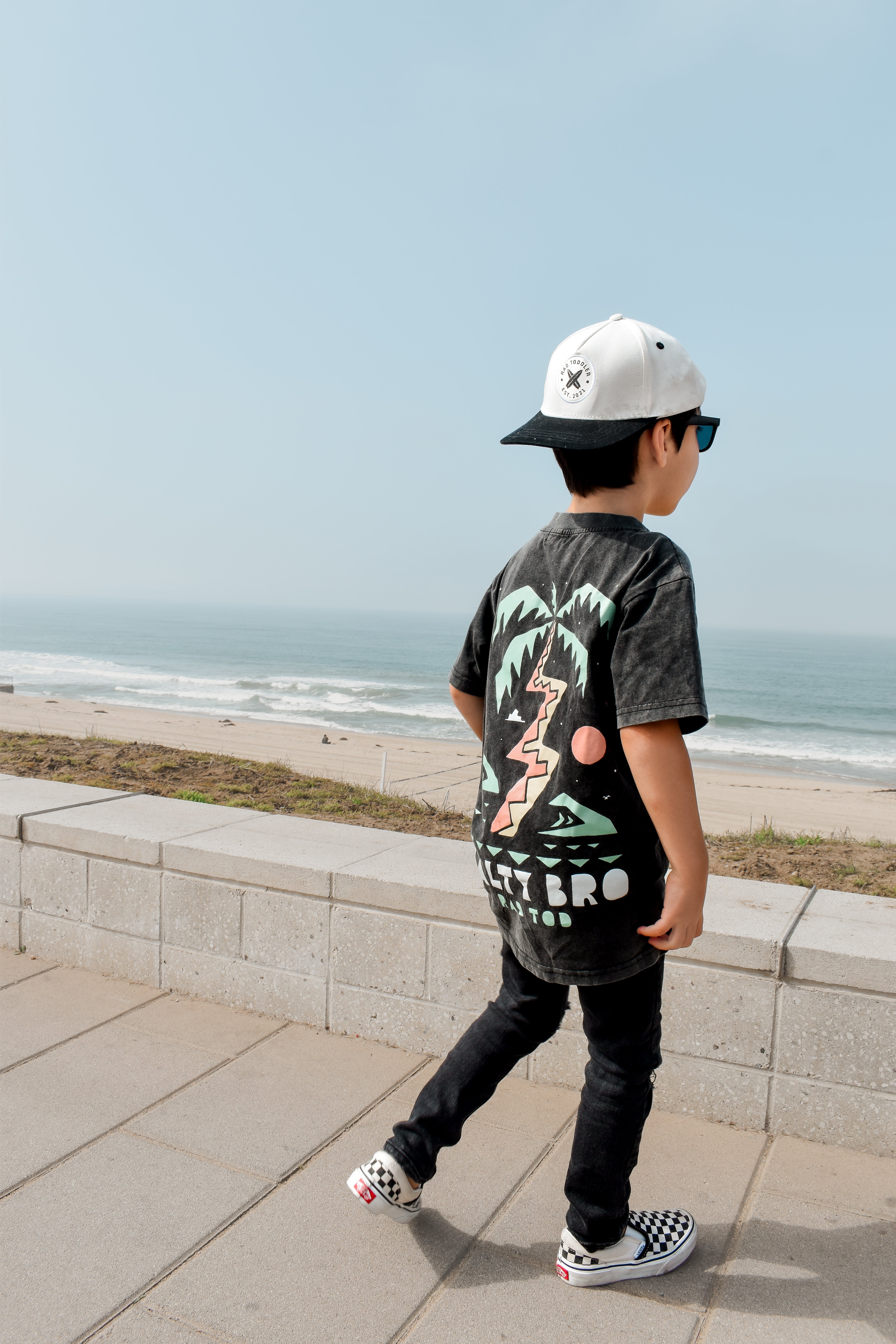 boy checking out the beach wearing Rad Toddler black acid wash toddler tee with bold 'Salty Bro' text in playful, beach style lettering
