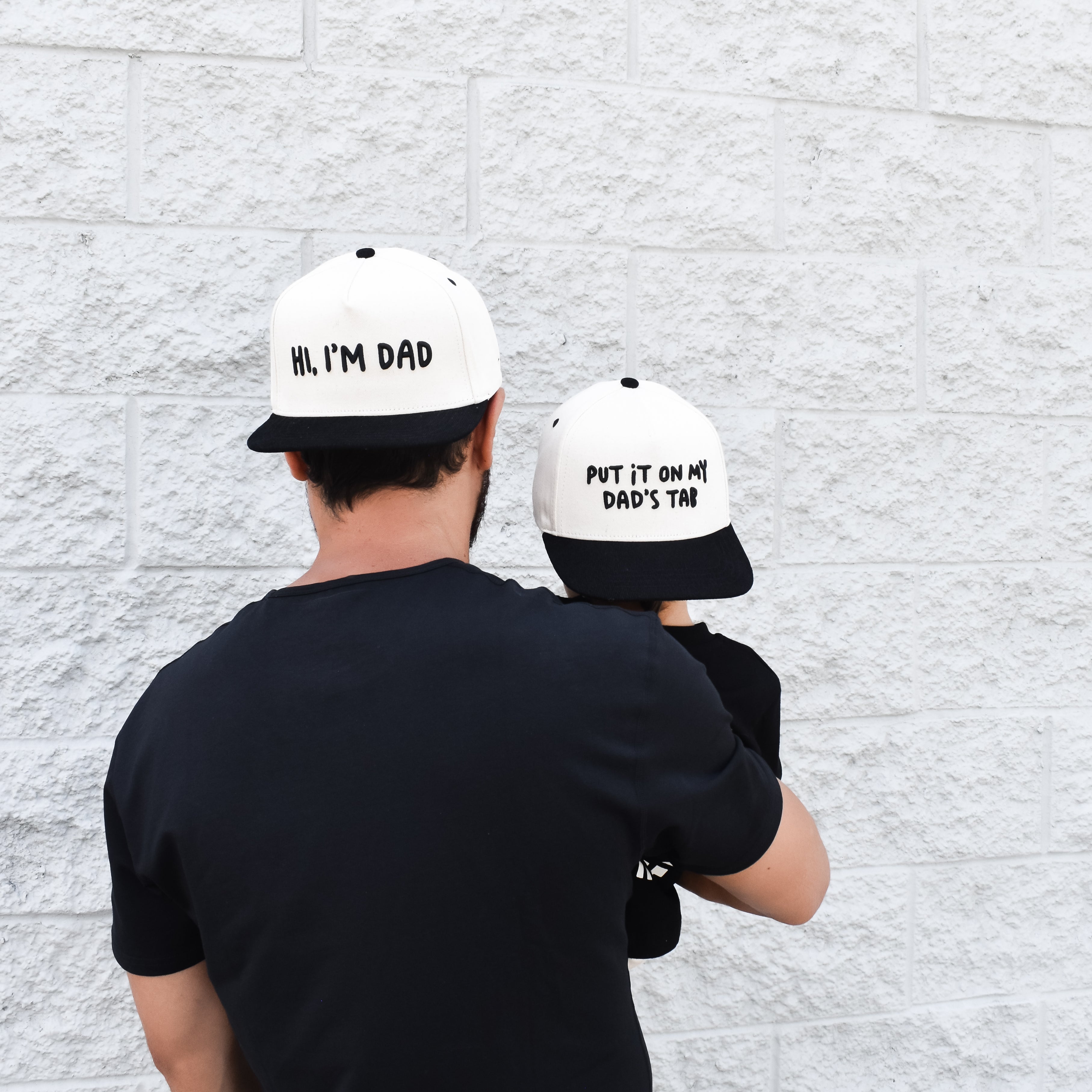 Dad wearing Hi, I’m Dad snapback outdoors while spending time with child.