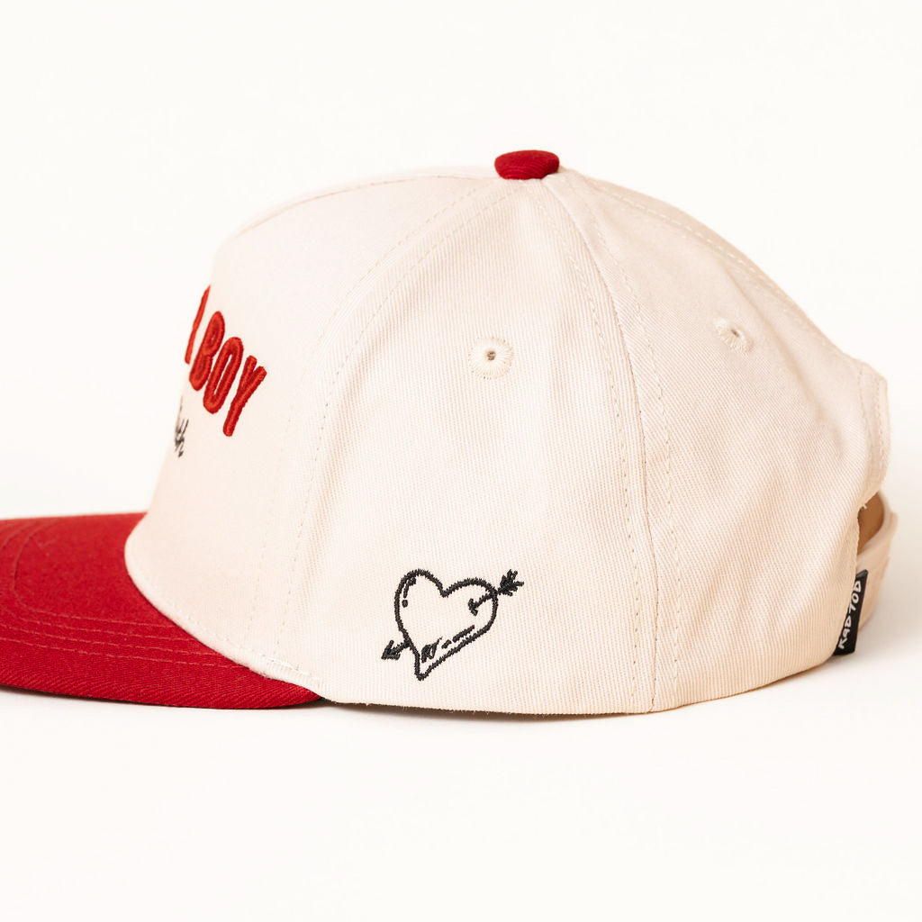 Beige cap with red brim and embroidered heart design on a white background