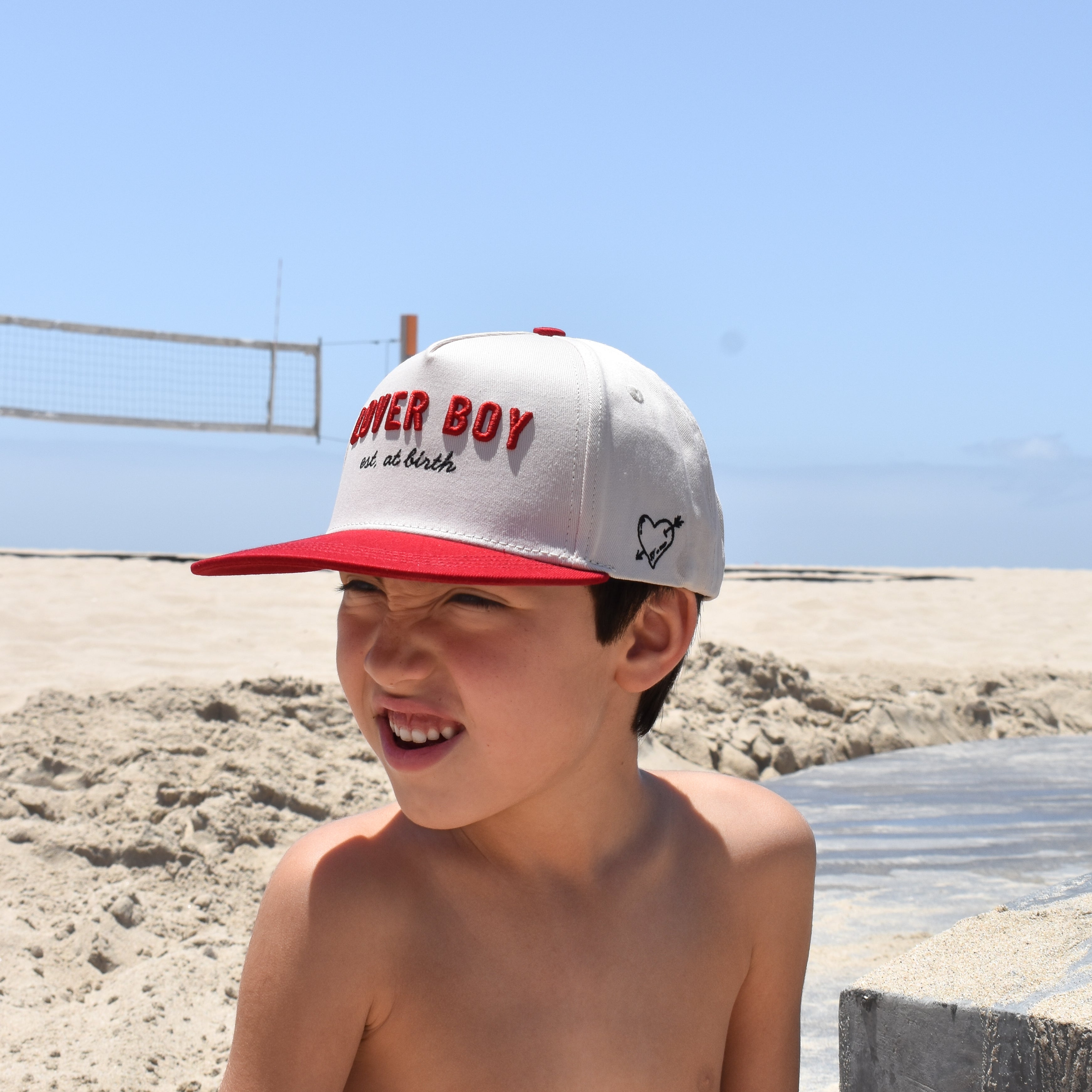 Young boy wearing a cap with Lover Boy hat on a beach