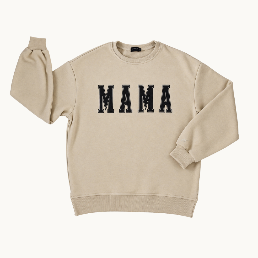 A beige crewneck sweatshirt featuring the word 'MAMA' printed across the chest in black varsity-style block letters with white outlines, displayed on a clean off-white background.