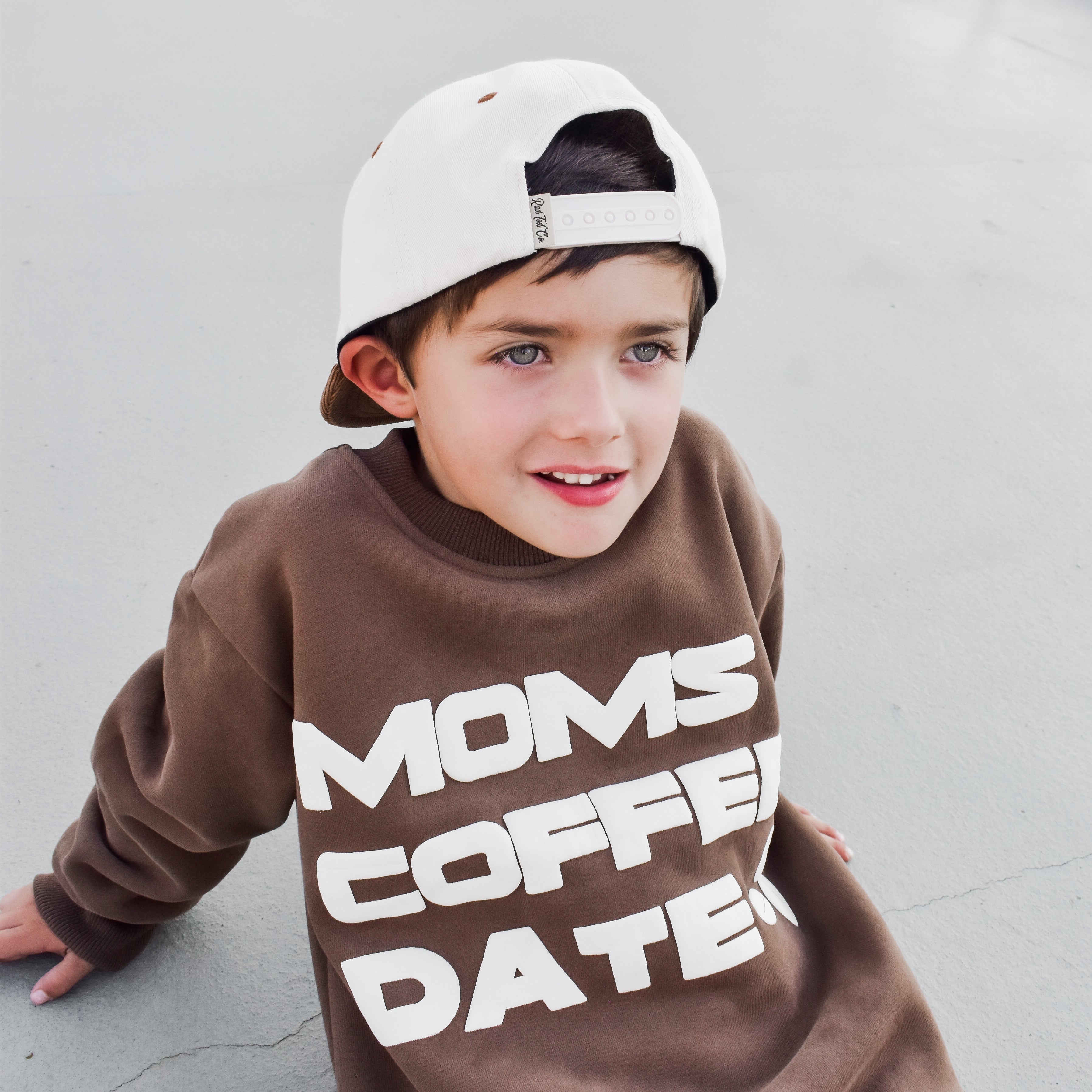 boy happily wearing coffee-brown “Mom’s Coffee Date” crewneck with bold off-white lettering, slightly oversized fit.