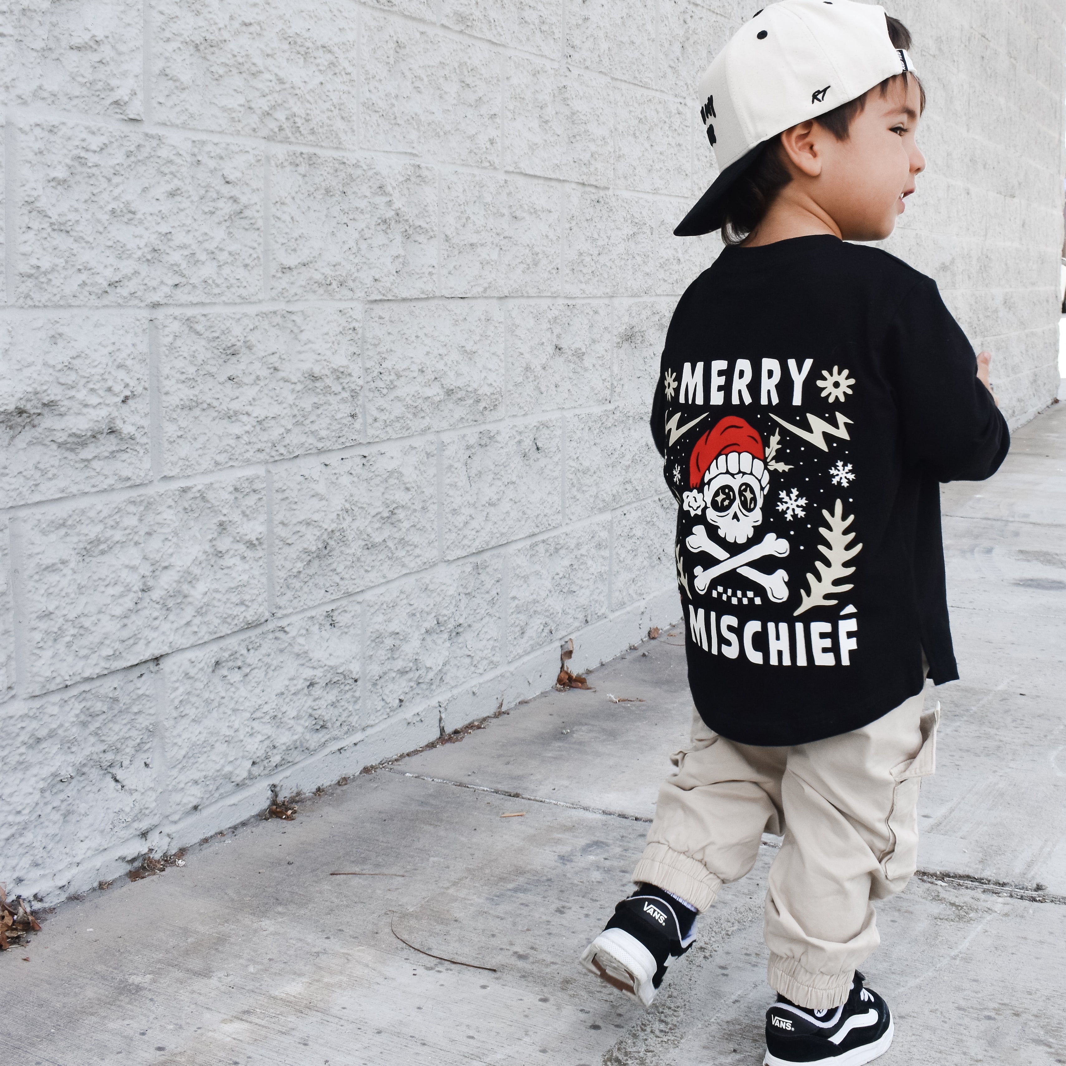 Child wearing a black t-shirt with a graphic design, walking on a sidewalk.
