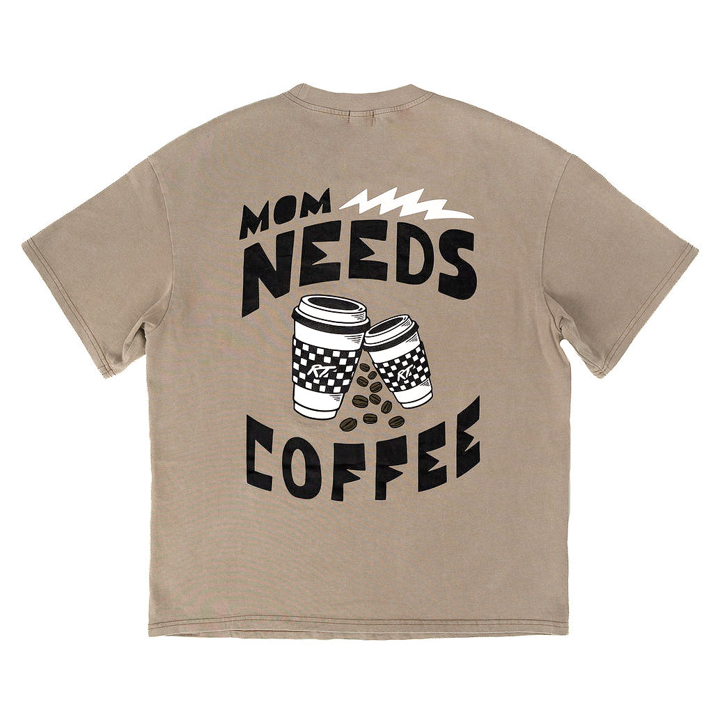 A beige short-sleeve t-shirt shown from the back, featuring a black graphic print that reads 'MOM NEEDS COFFEE' with two coffee cups and coffee beans.