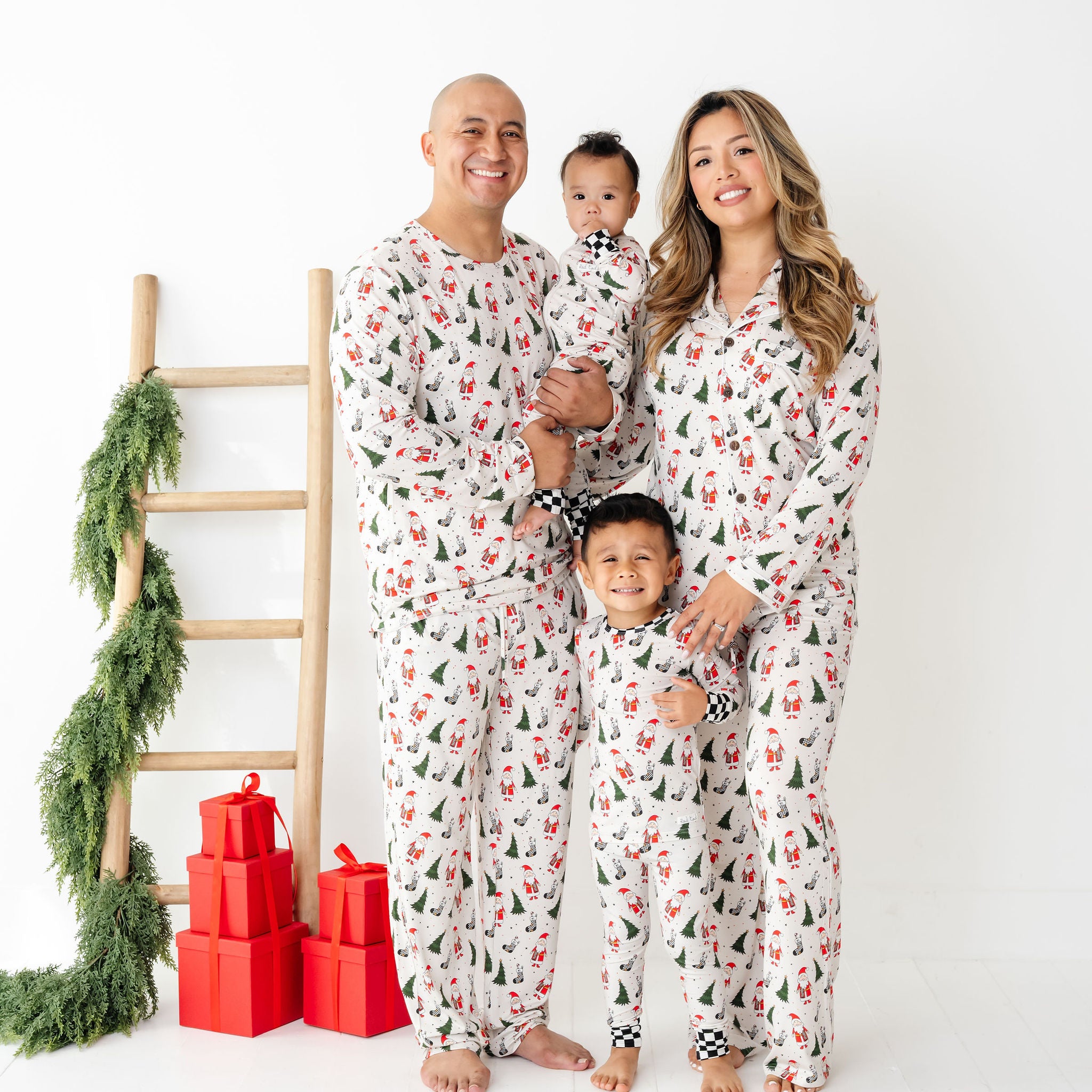 Family of four wearing matching pajamas with a Christmas tree and presents in the background while wearing Merry Everything Bamboo by RAD TODDLER