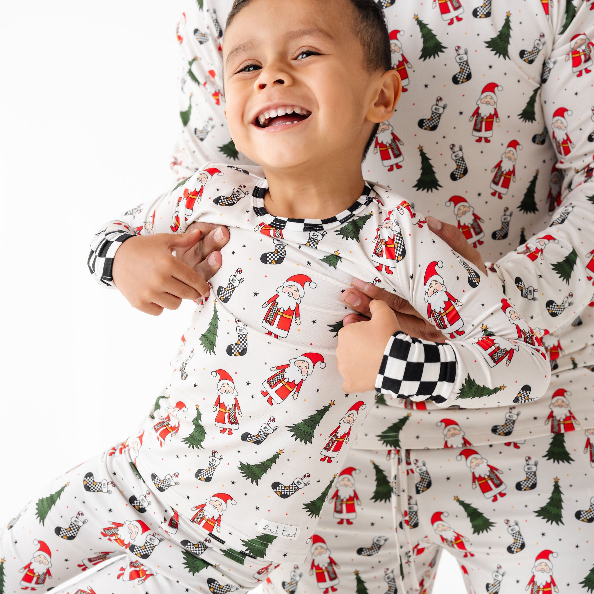 Two children wearing matching Christmas-themed pajamas with Santa Claus and trees.