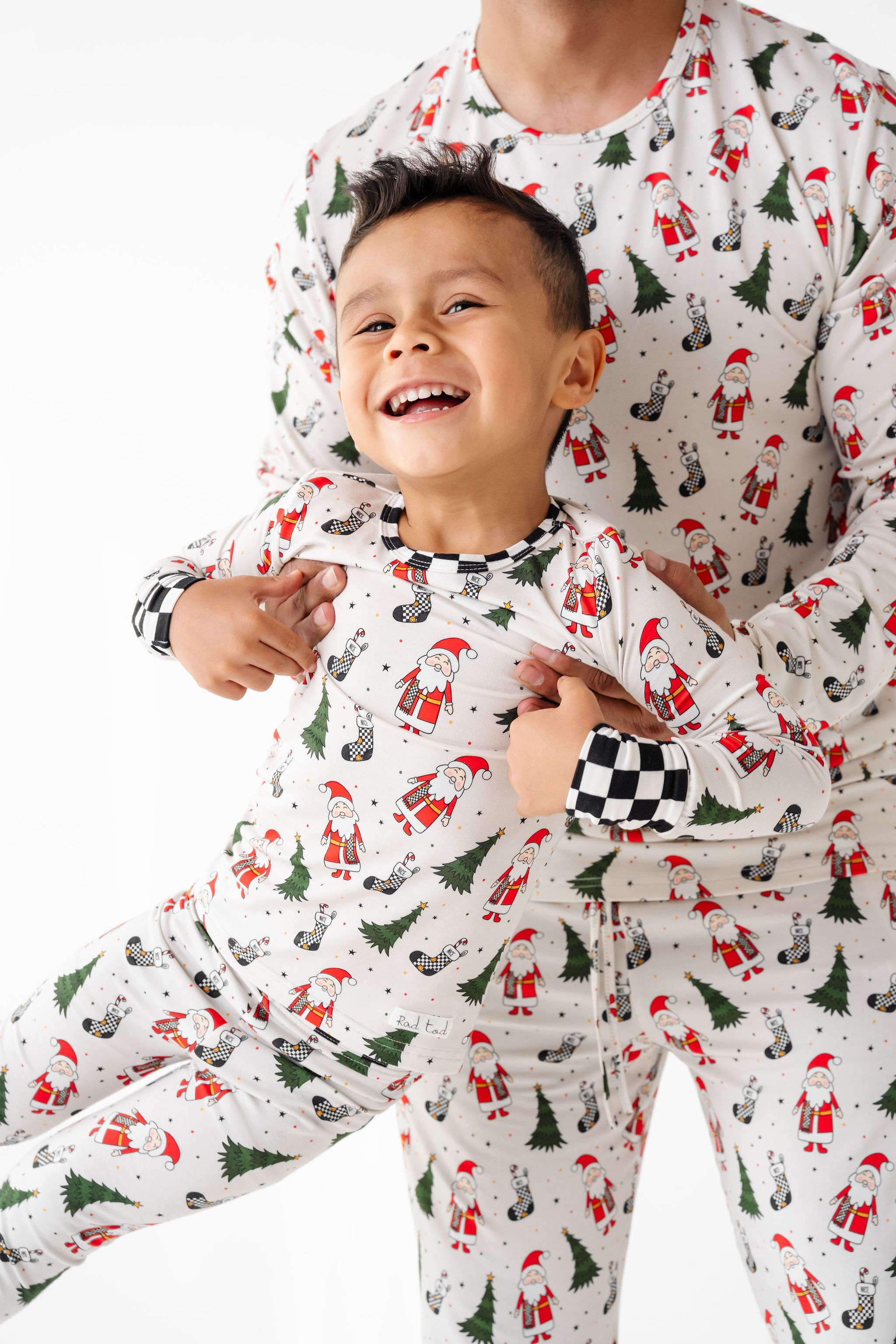 Two children wearing matching Christmas-themed pajamas with Santa Claus and trees.