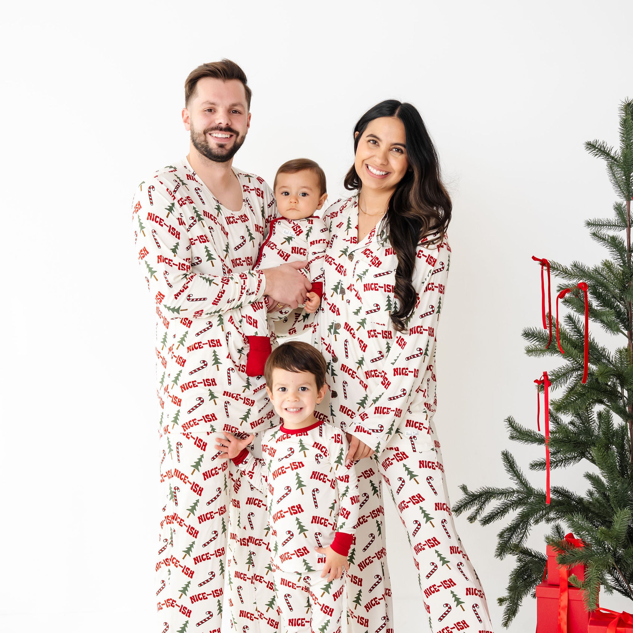 Family of four wearing matching pajamas in front of a Christmas tree with presents.