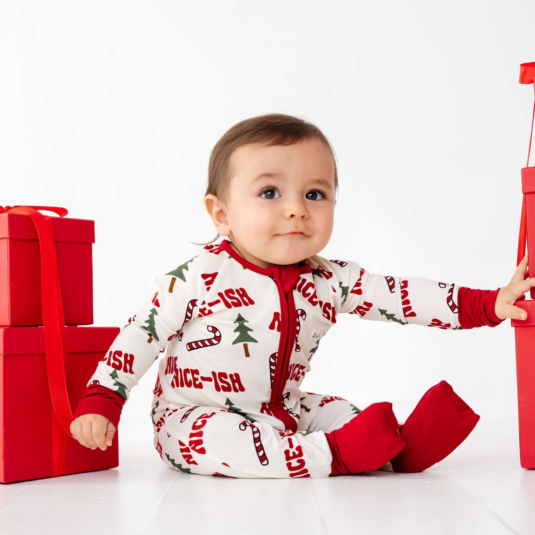 Baby in Christmas-themed outfit with presents on a white background