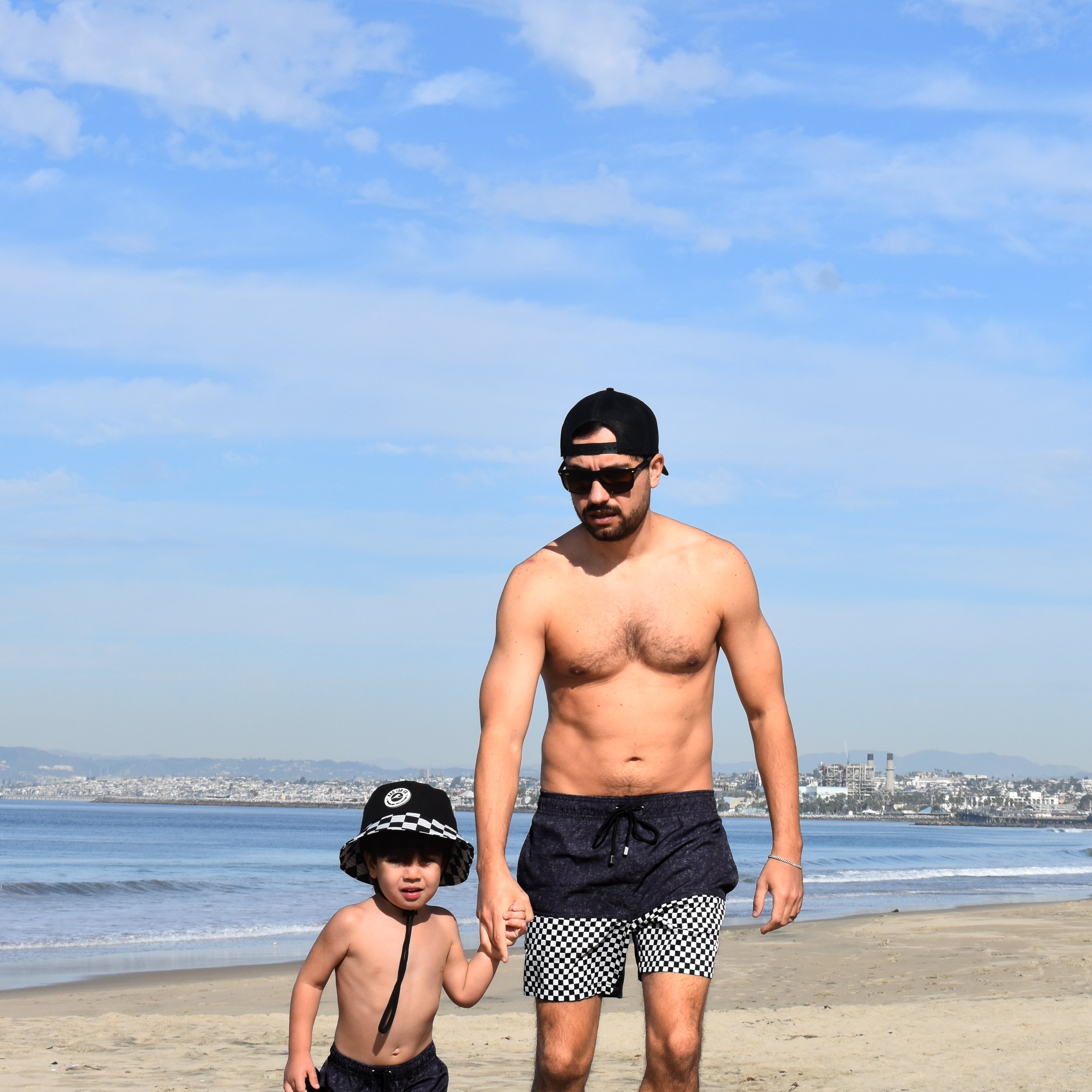 Man and child standing on a beach with ocean and sky in the background wearing matching Onyx Swimmie Shorts
