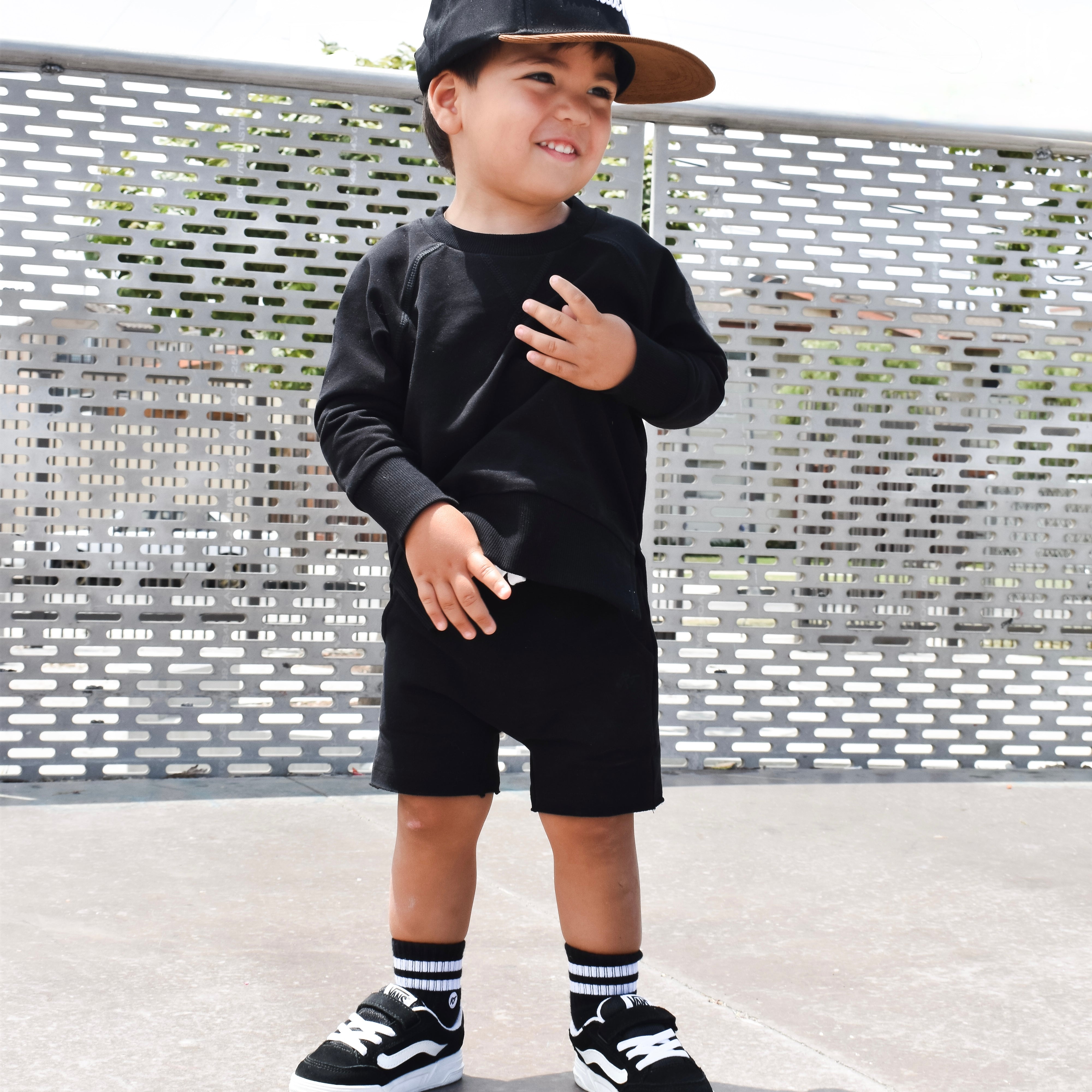 Child wearing a black outfit with a cap, standing on a textured surface.