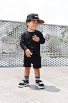 Child wearing a black outfit with a cap, standing on a textured surface.