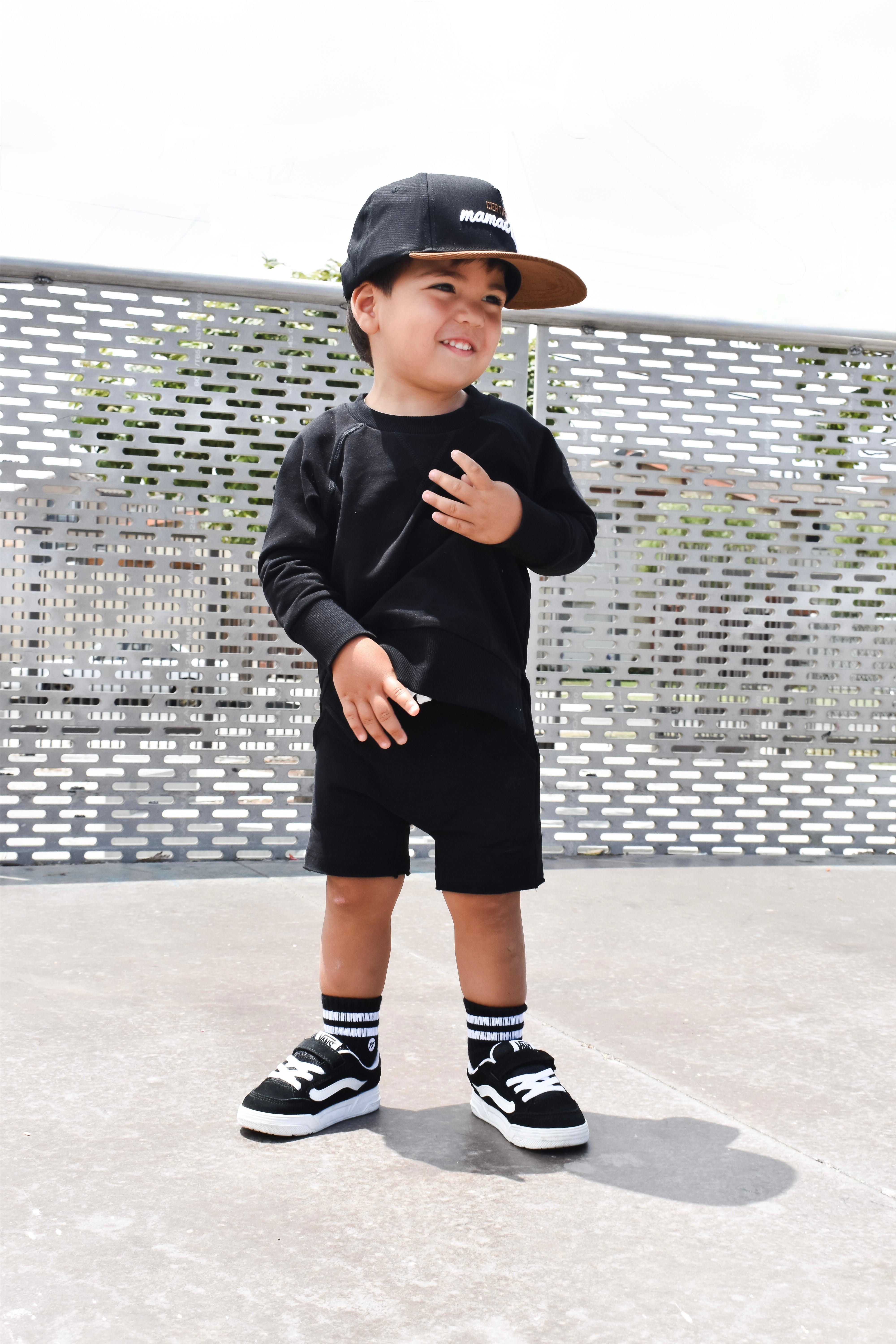 Child wearing a black outfit with a cap, standing on a textured surface.