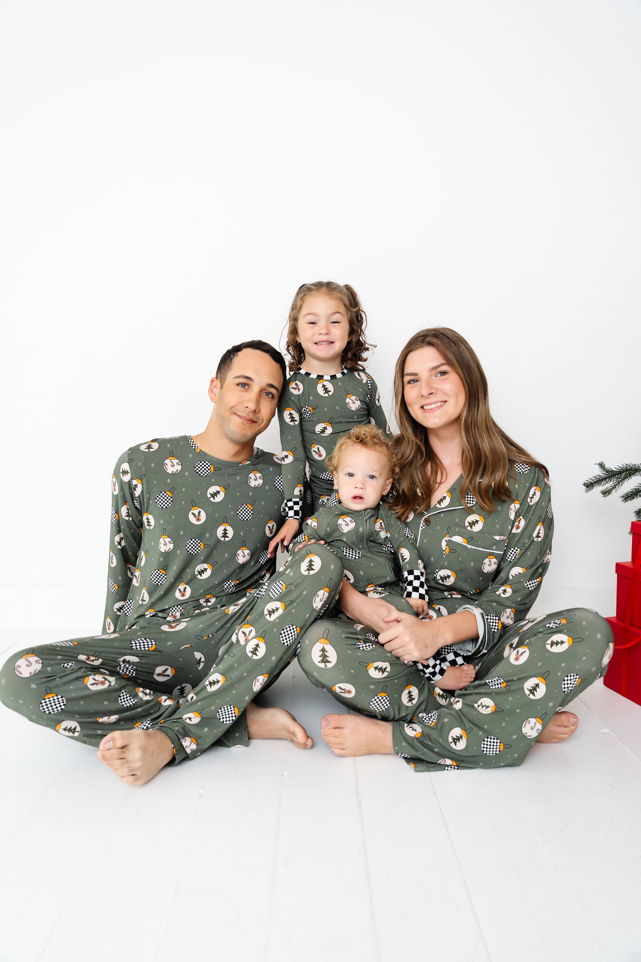 Family of four wearing matching green pajamas with a Christmas tree pattern on a white background by RAD TODDLER