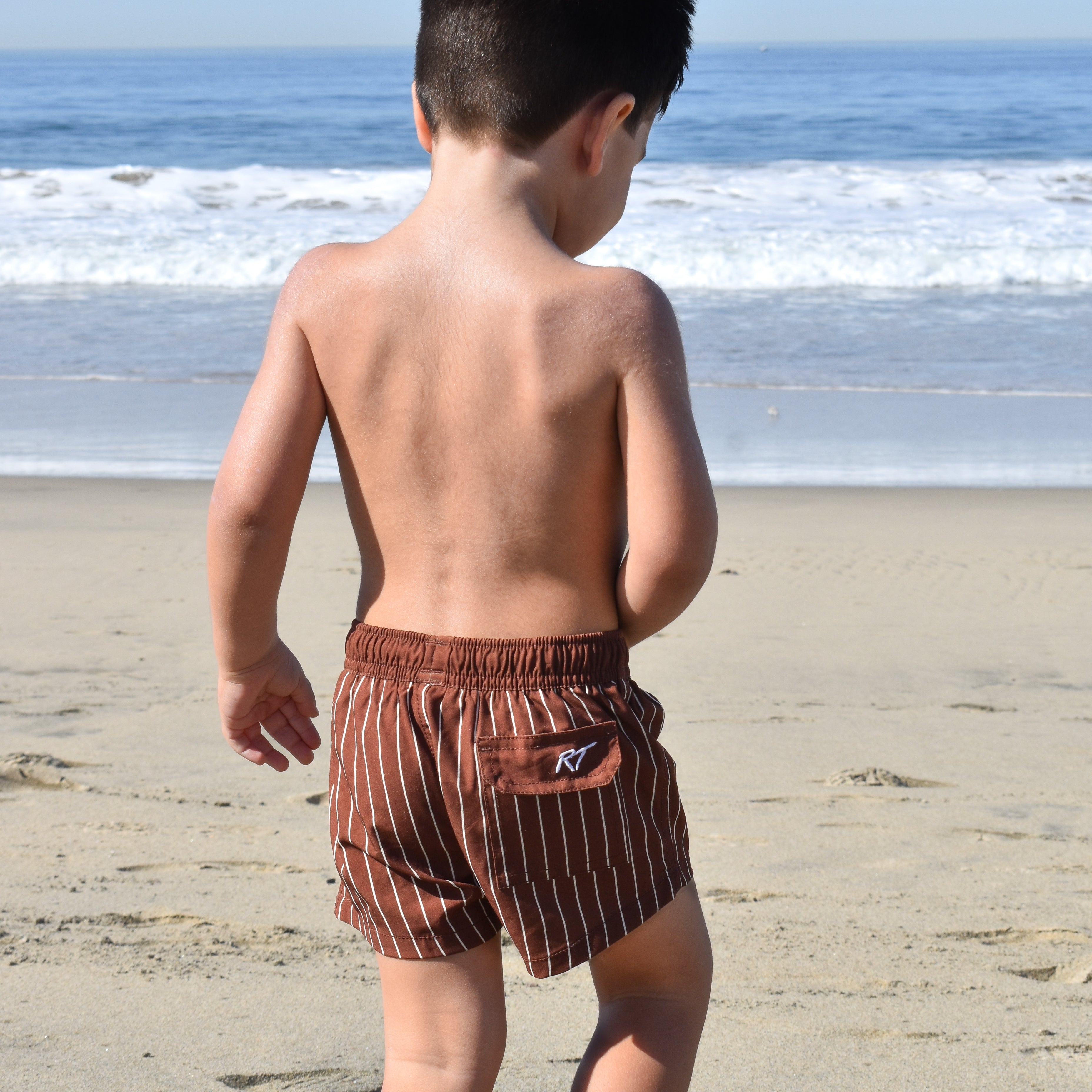 Child wearing brown striped swim shorts on a beach