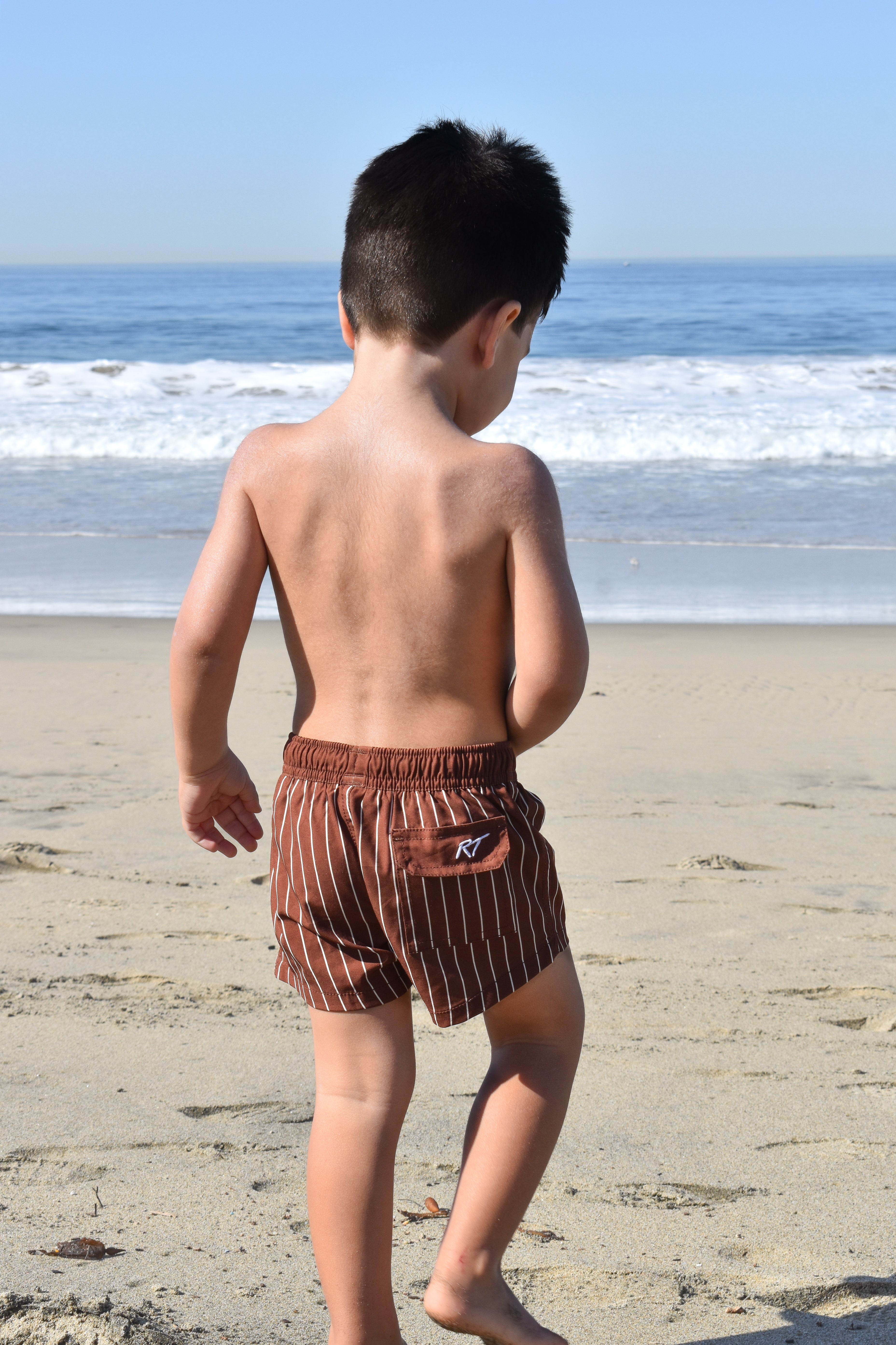 Child wearing brown striped swim shorts on a beach