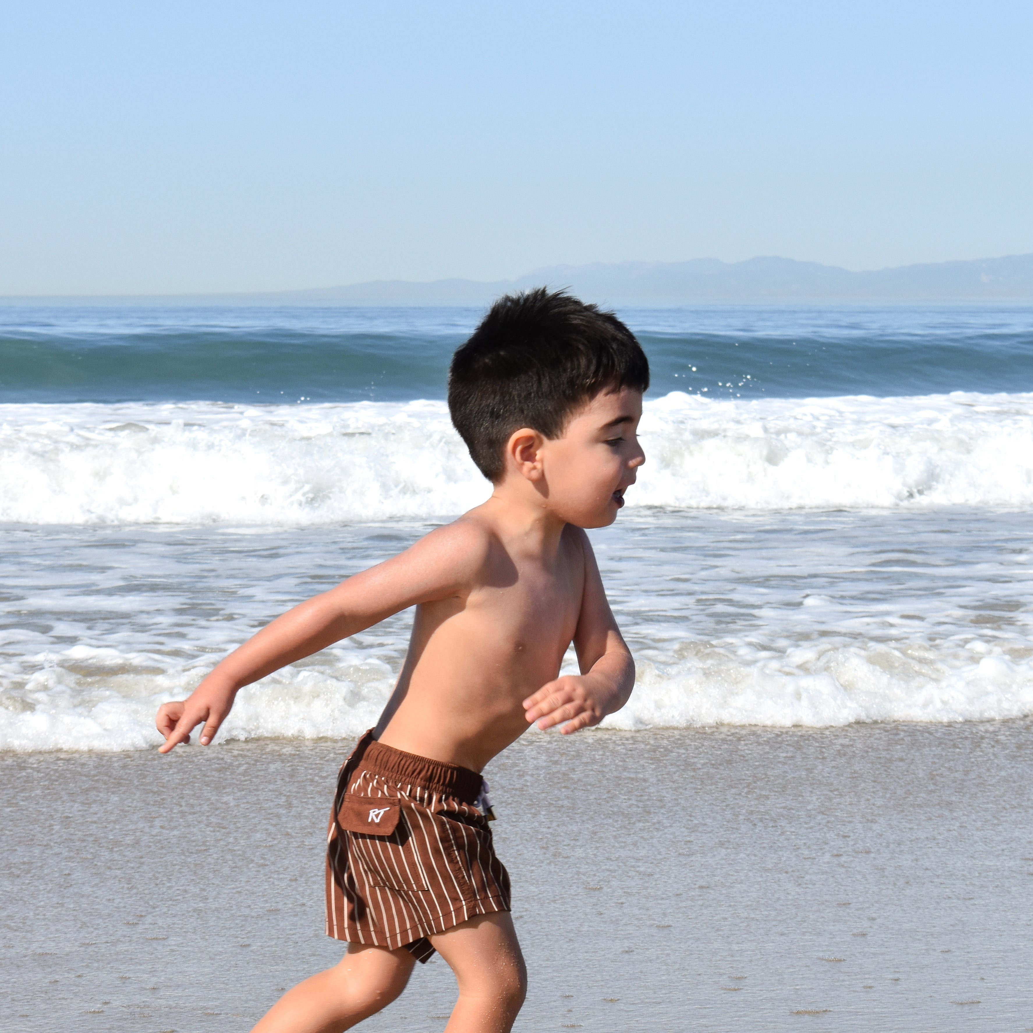 boy wearing Pinstripe Espresso swimmies by rad toddler on a beach