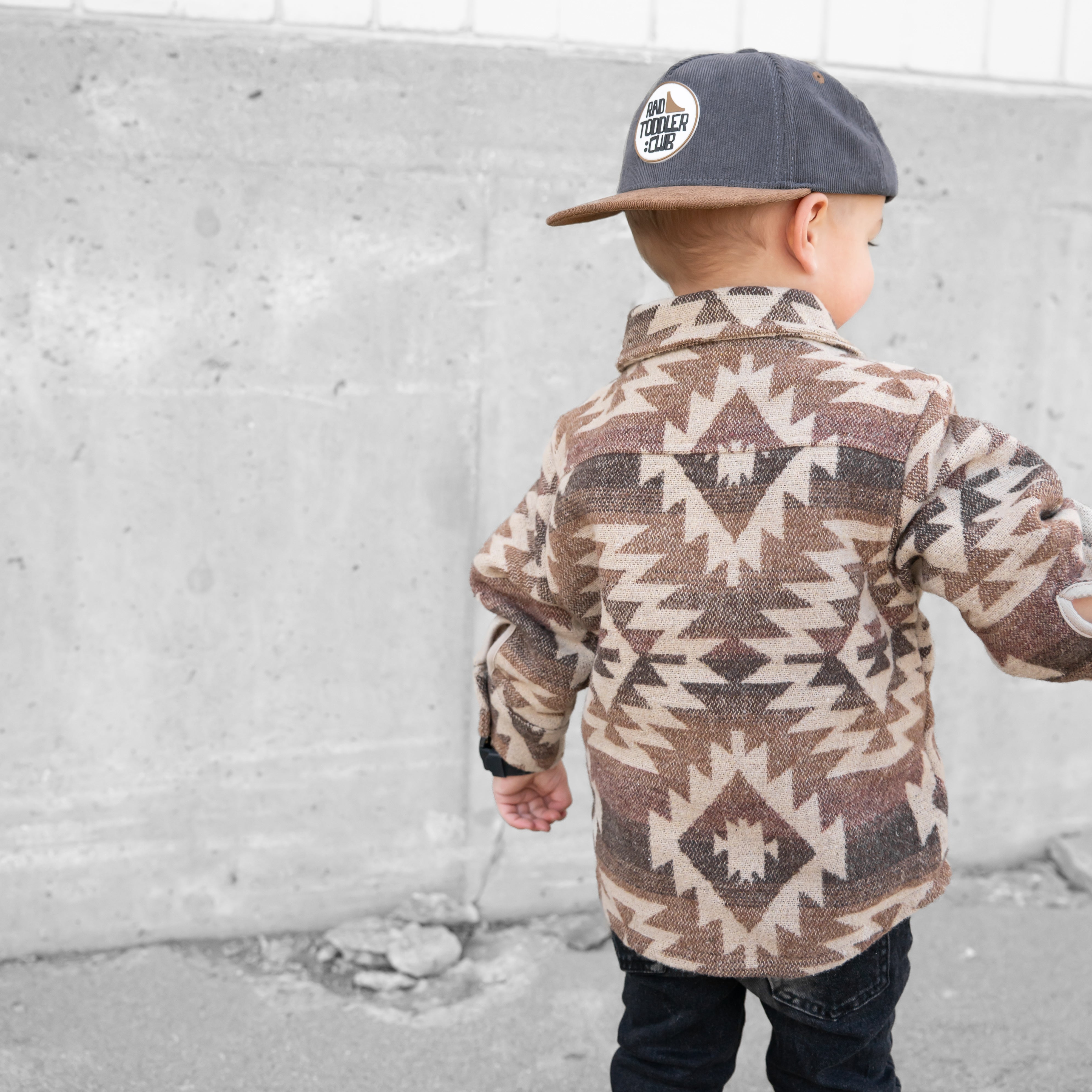 Child wearing RAD TODDLER Skate Club snapback outdoors while playing.