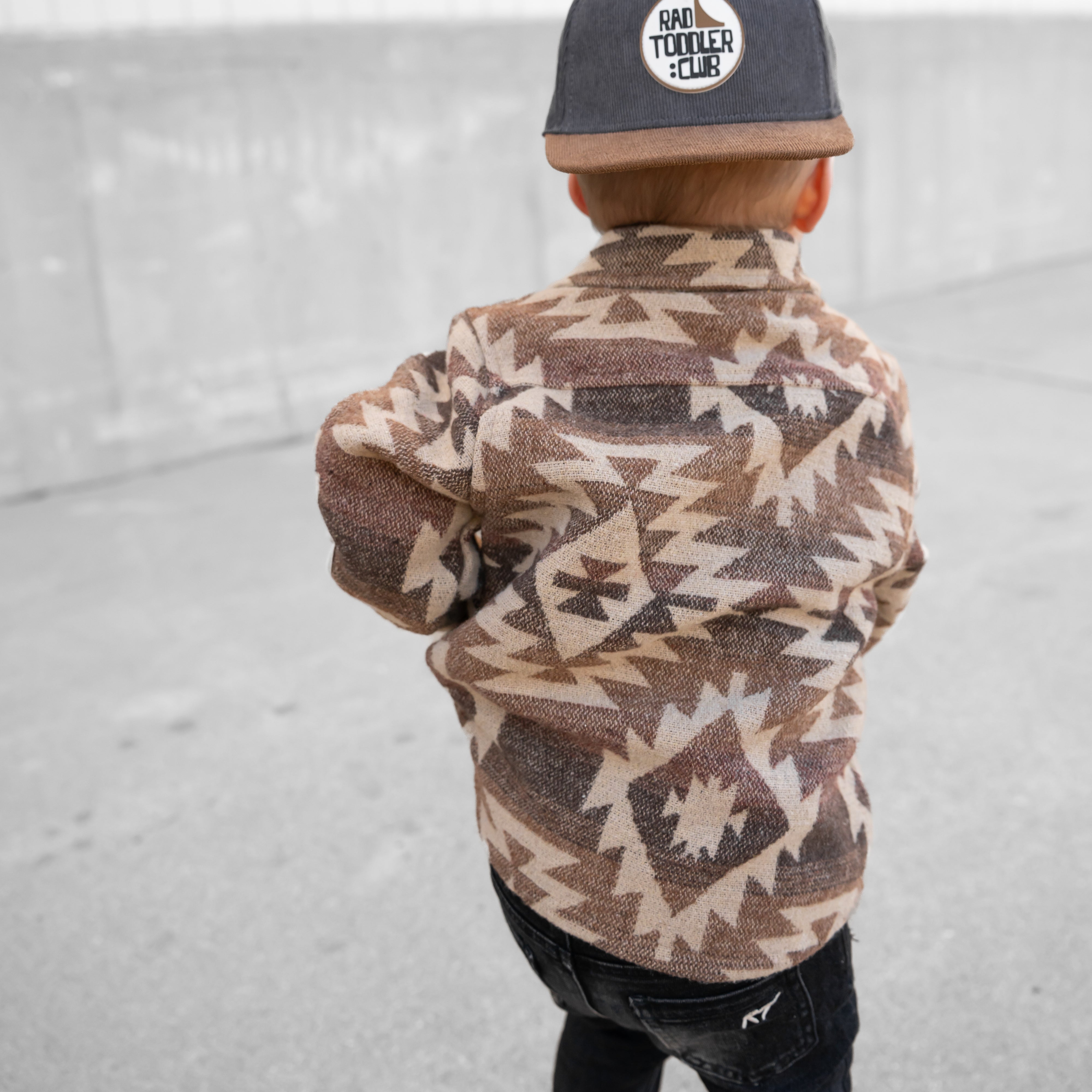 Child wearing a patterned jacket and cap on a light gray background