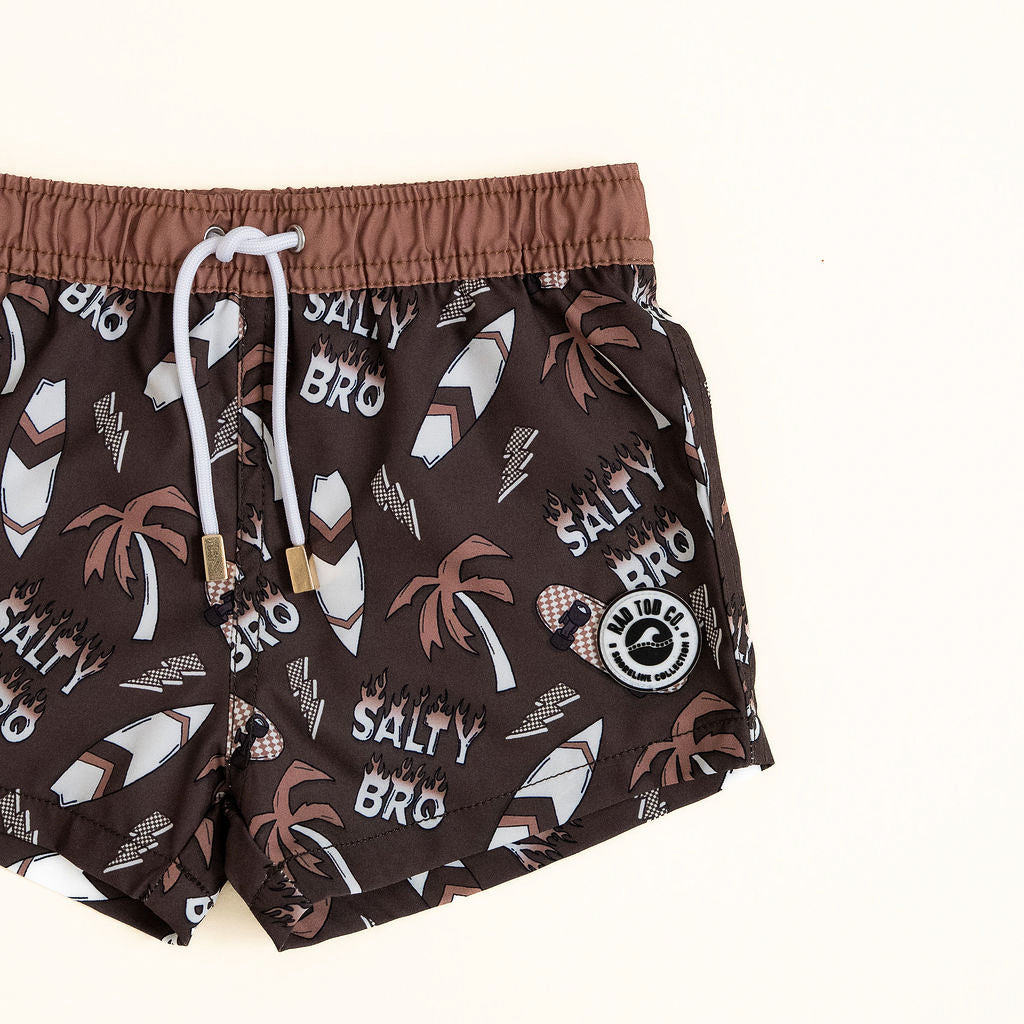 Brown swim shorts with palm tree and 'Salty Bro' print on a white background