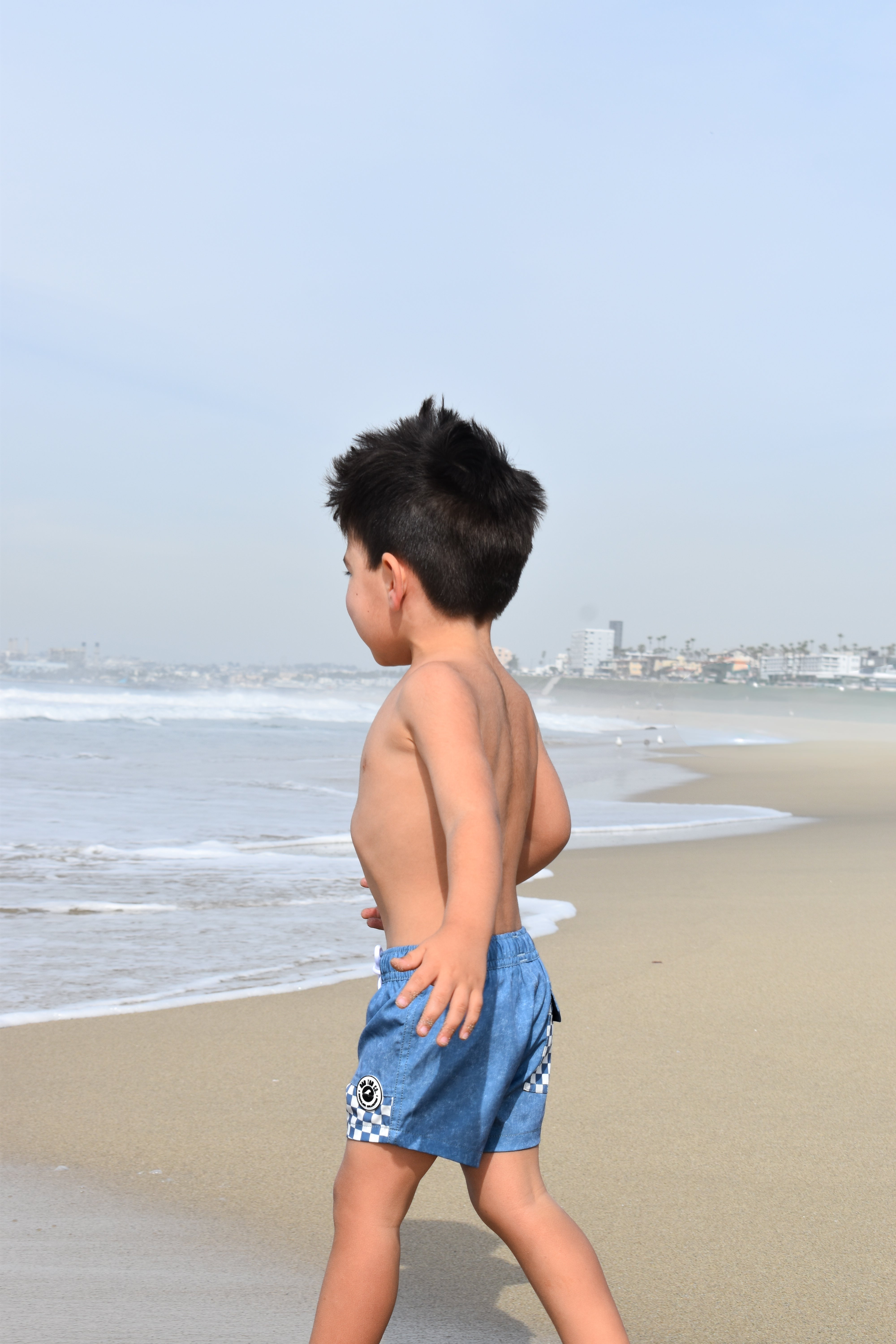 Child in blue swim shorts standing on a beach with ocean and skyline in the background