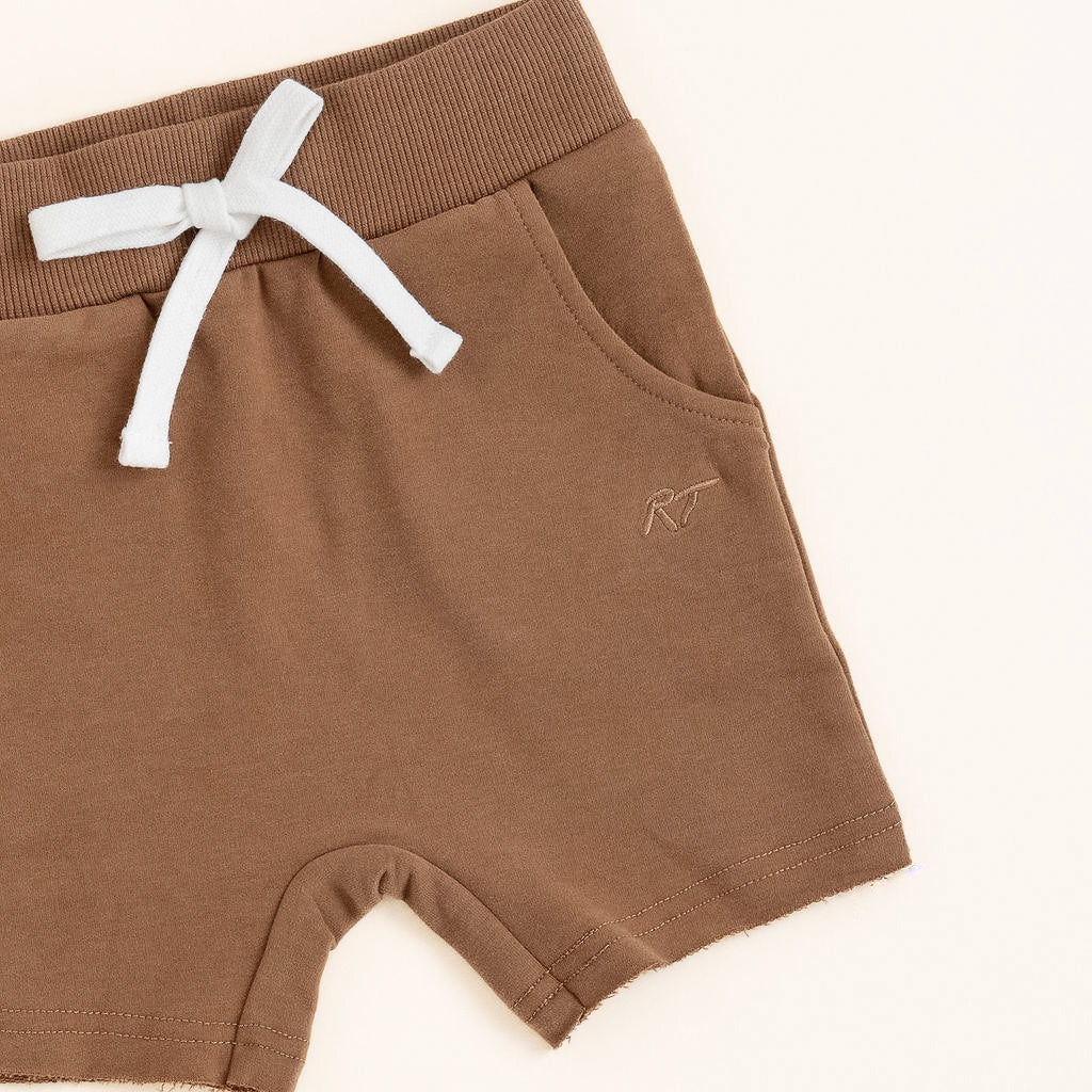 Flat lay of almond toddler shorts from the Core Collection with adjustable waistband and front pockets from the side.