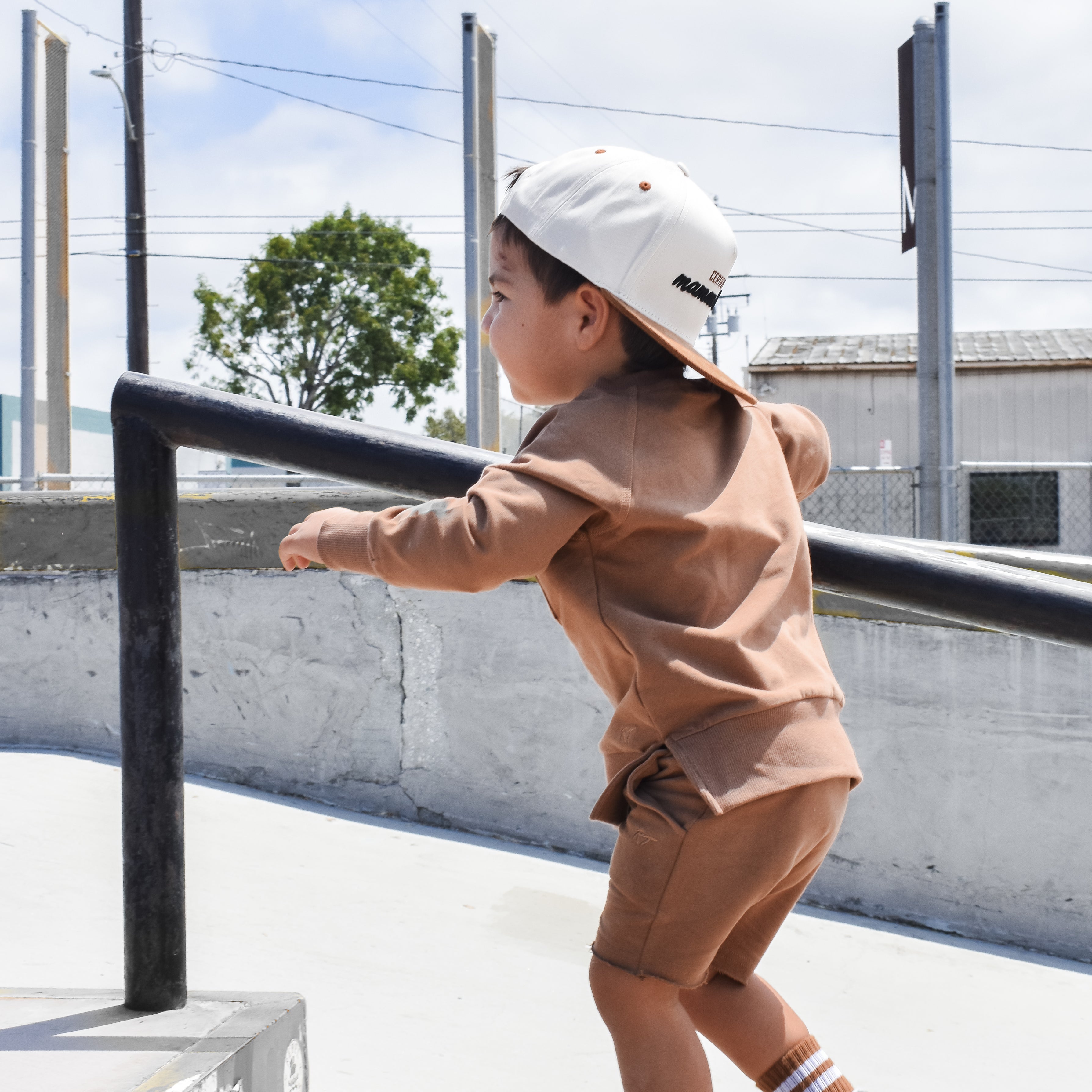 Young boy wearing almond Core Collection toddler shorts, at the skatepark and showcasing the relaxed, above-the-knee fit.