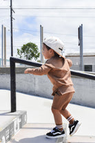 Young boy wearing almond Core Collection toddler shorts, at the skatepark and showcasing the relaxed, above-the-knee fit.