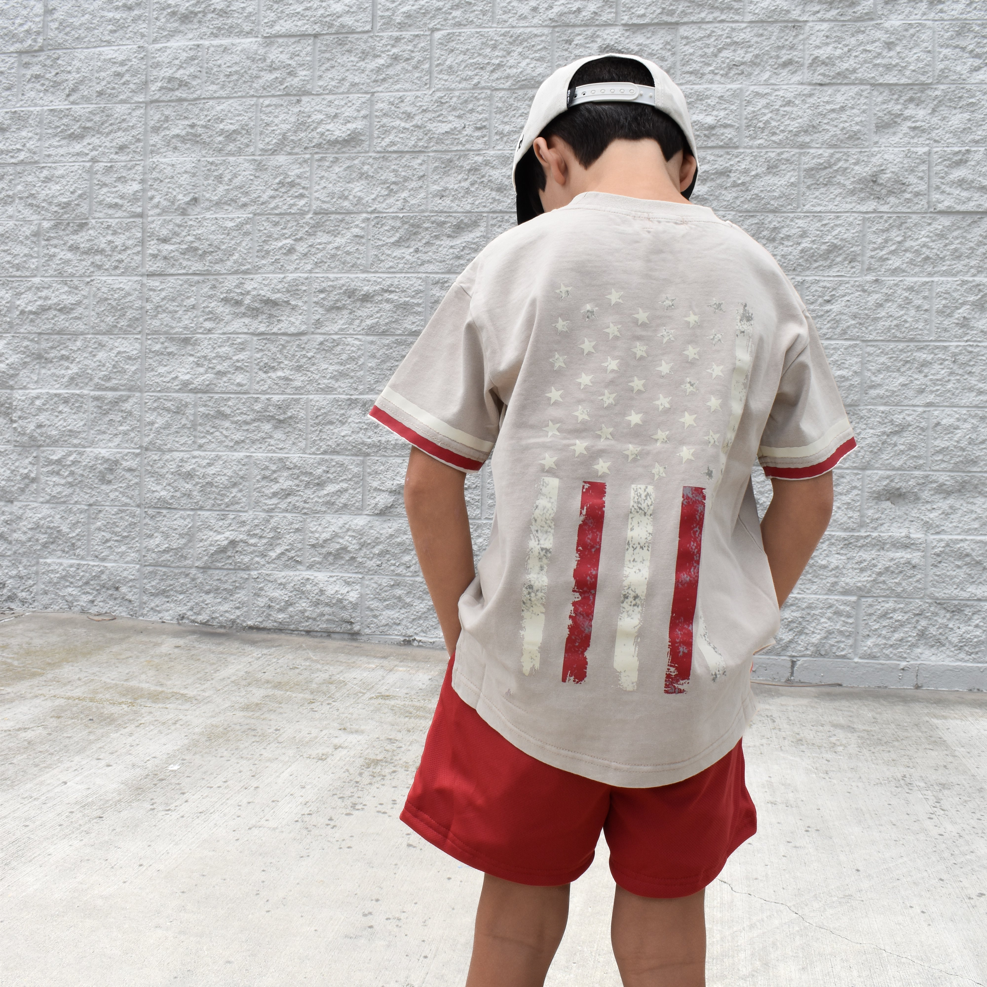 Kid wearing the American Original Tee in a vintage beige color with classic Americana-inspired graphic design.