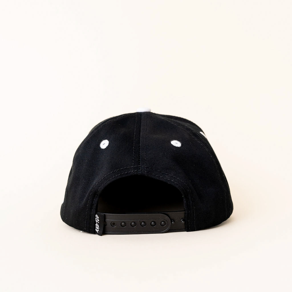A black snapback cap shown from the back, featuring white embroidered eyelets and a black adjustable strap with a small white brand tag.