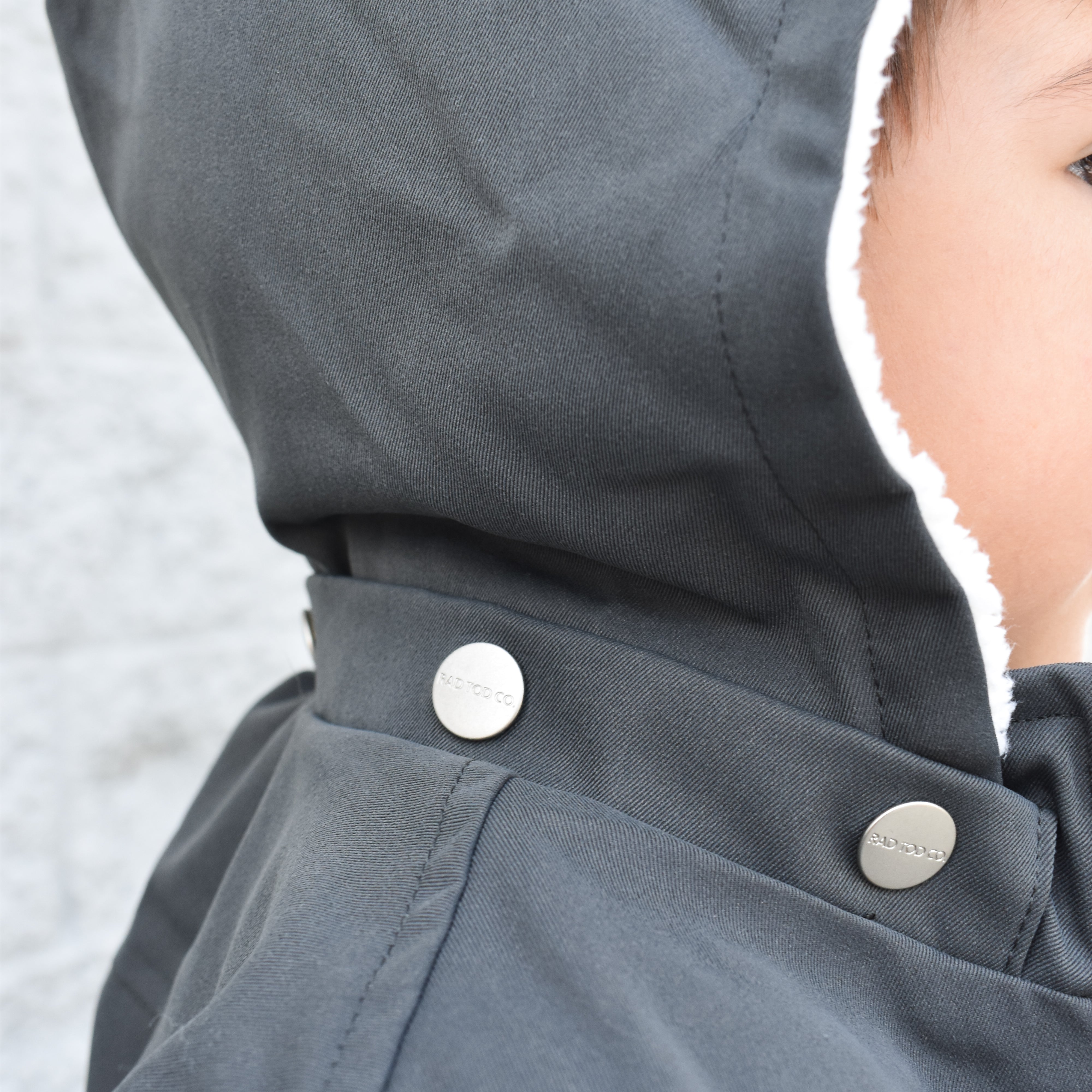 Close-up of a dark gray hooded jacket with buttons, featuring a blurred background.