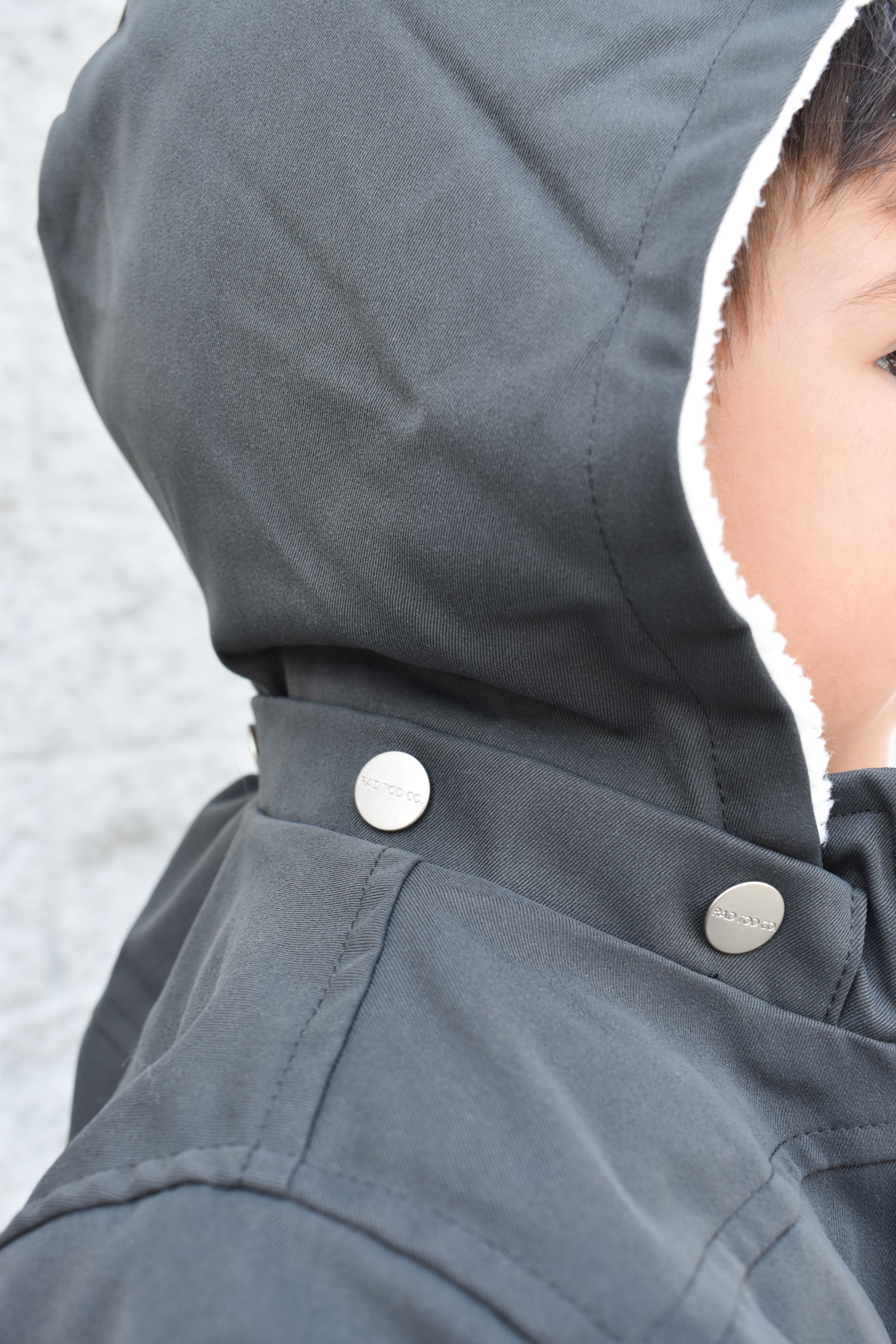 Close-up of a dark gray hooded jacket with buttons, featuring a blurred background.