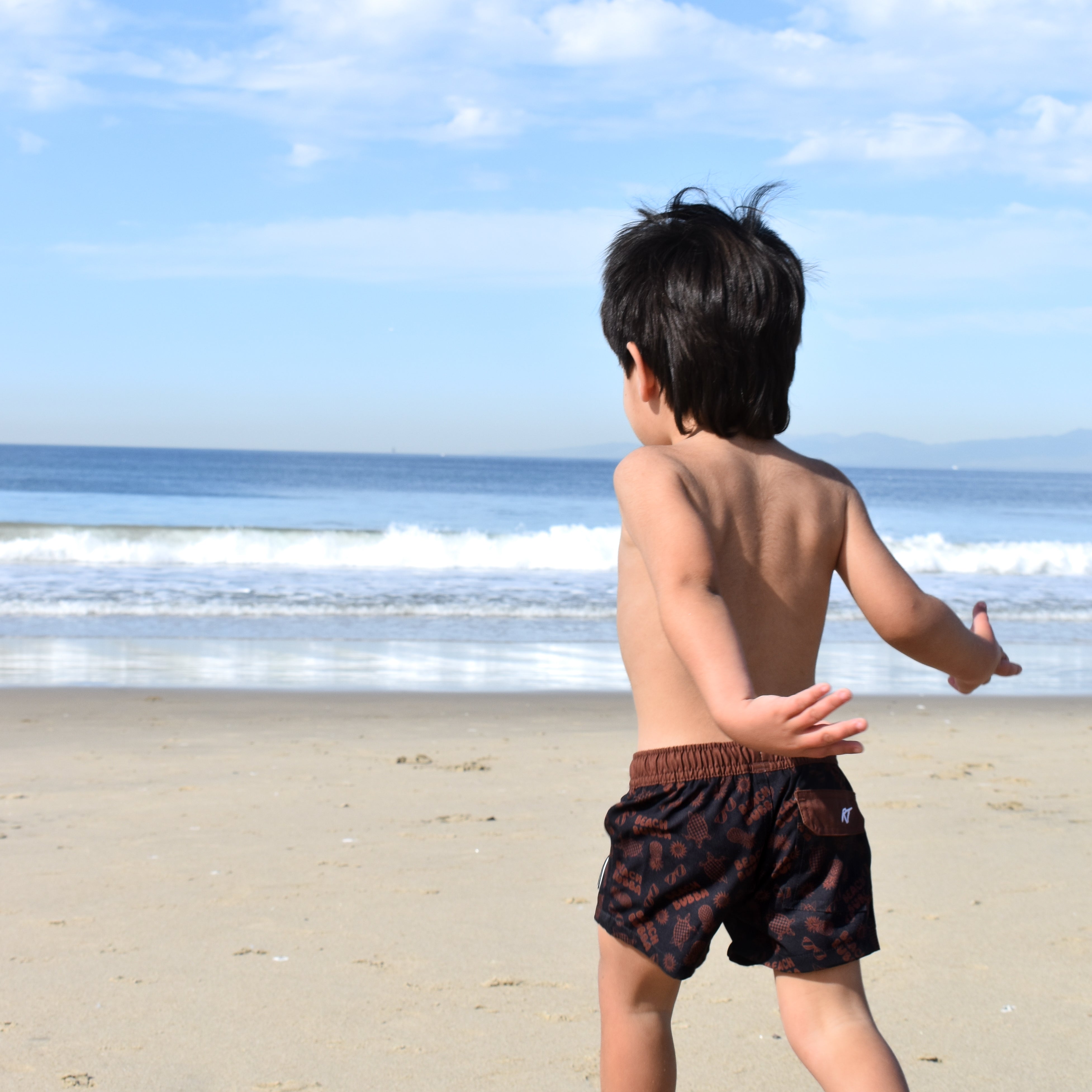 Child running on a sandy beach with ocean and blue sky in the background