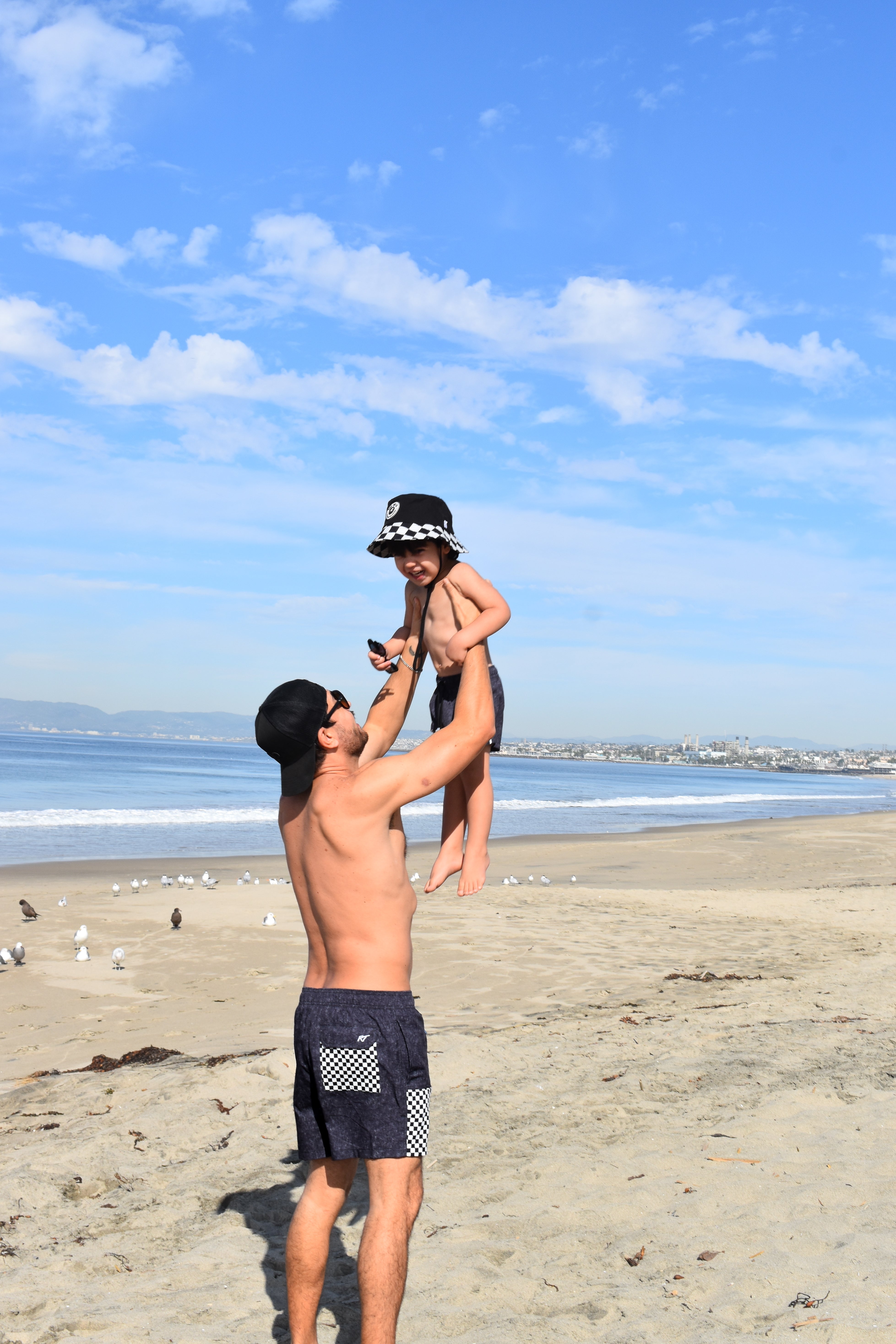 Man lifting child in the air on a beach with ocean and sky in the background