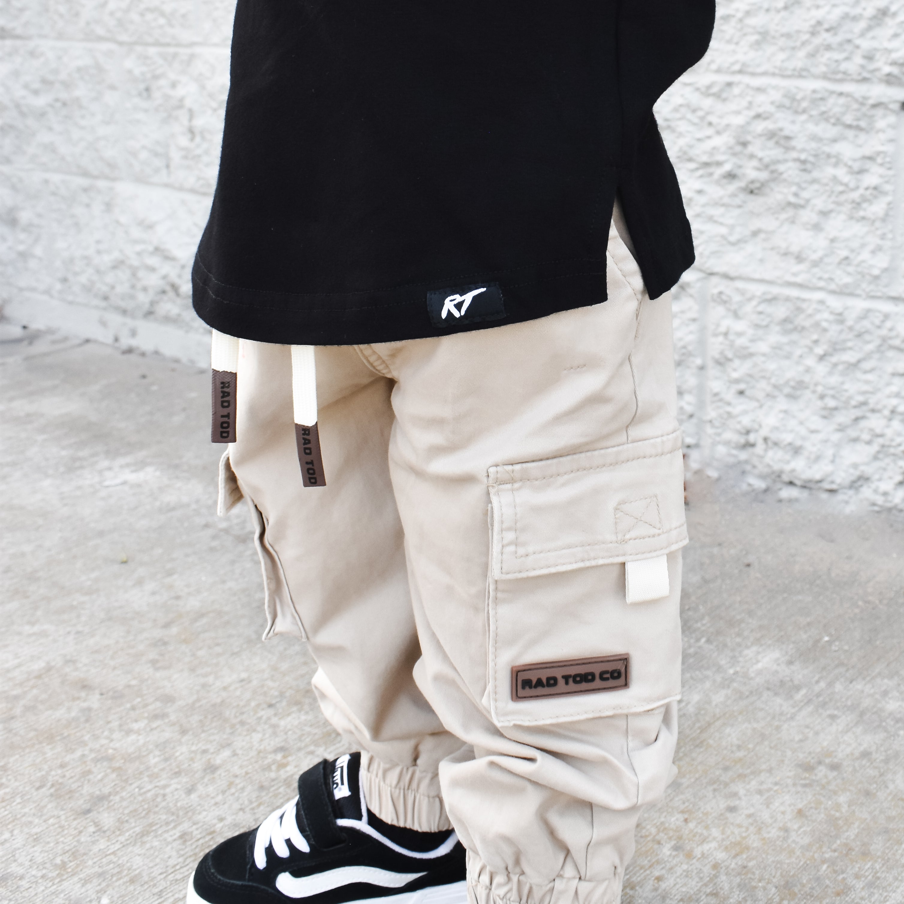 Person wearing beige cargo pants and black sneakers against a light gray background