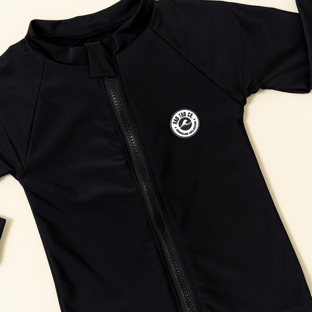Black zip-up shirt with a logo on a light beige background