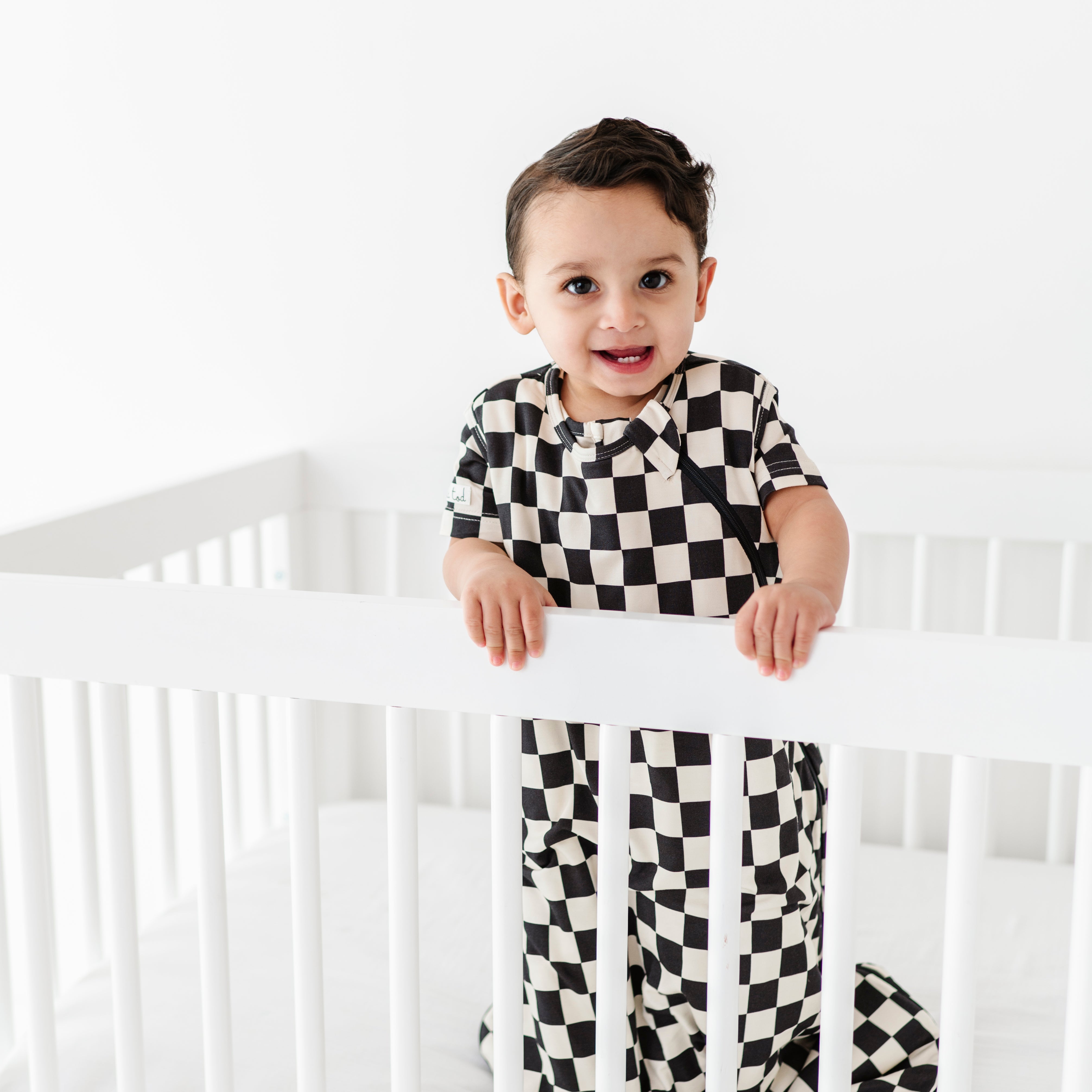 boy in crib wearing Bamboo sleep bag for toddlers in black and white checkered pattern, featuring a two-way zipper by Rad Toddler.