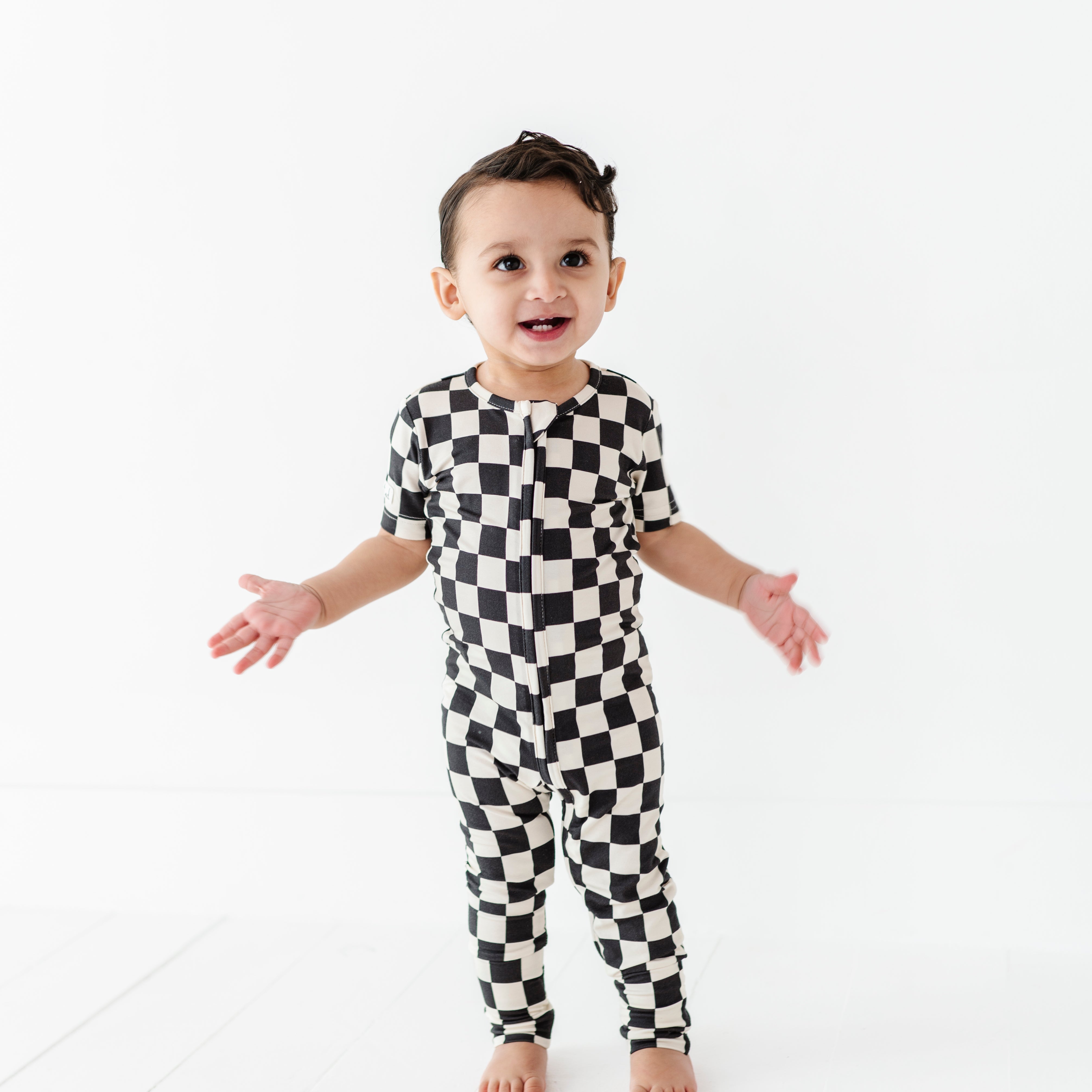 boy wearing Black and white checkered bamboo short sleeve onesie for toddlers, featuring a two-way zipper and optional foldover footies by Rad Toddler.