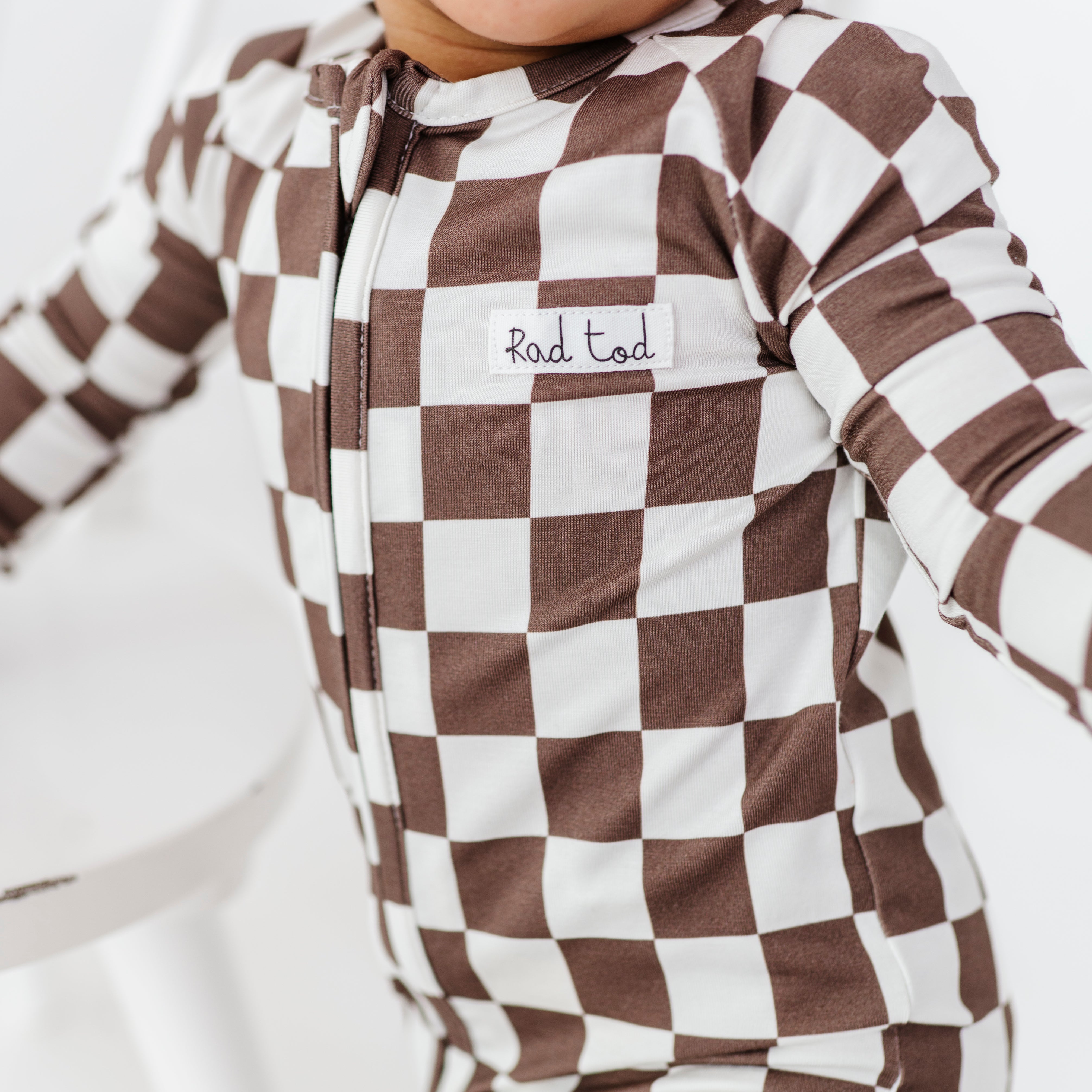 boy smiling wearing Bronze and white checkered bamboo pajamas for toddlers, featuring a two-way zipper and foldover footies by Rad Toddler.