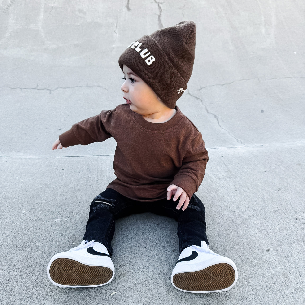 Child wearing a brown outfit with a matching beanie on a concrete surface