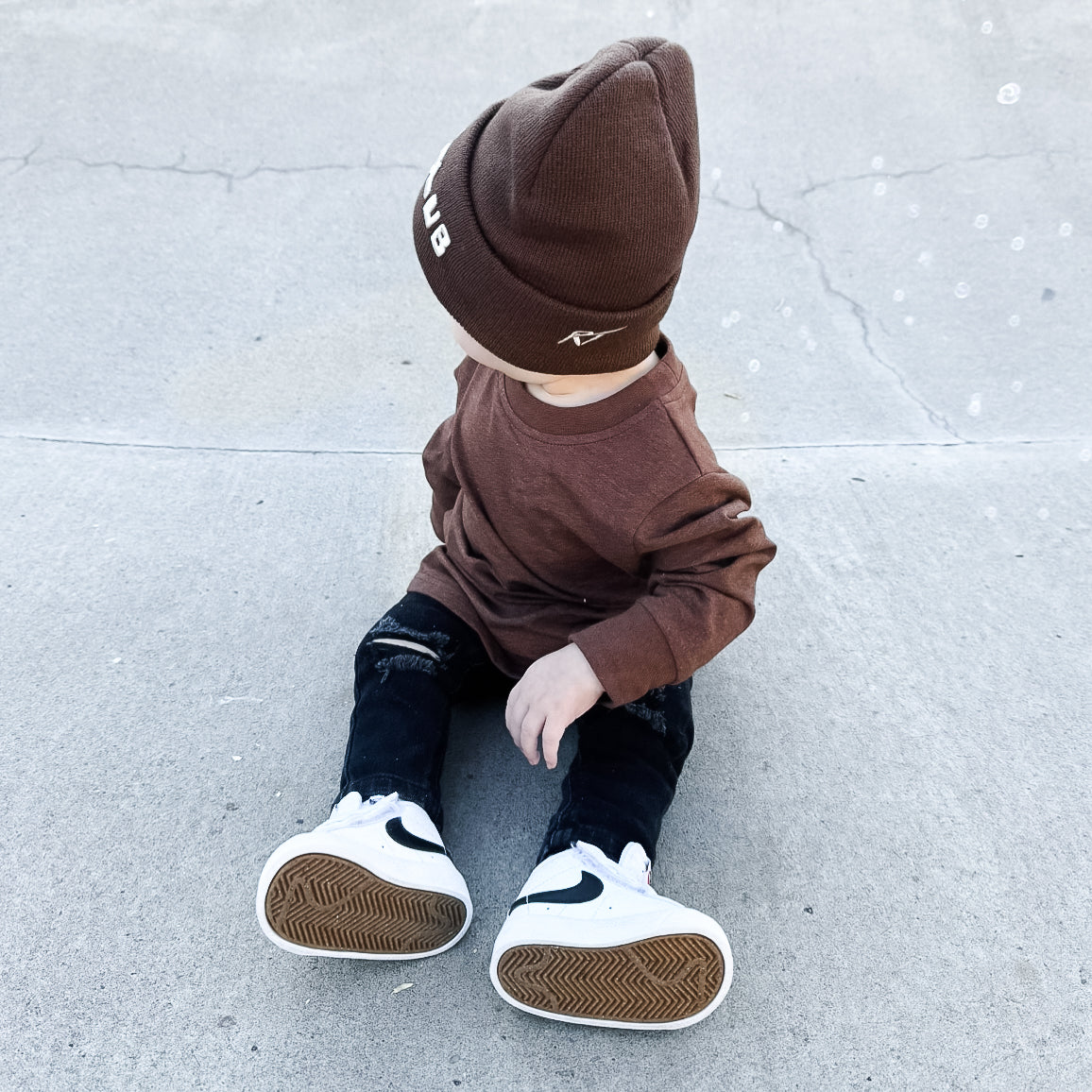 Child wearing a brown outfit with a beanie on a light gray concrete surface