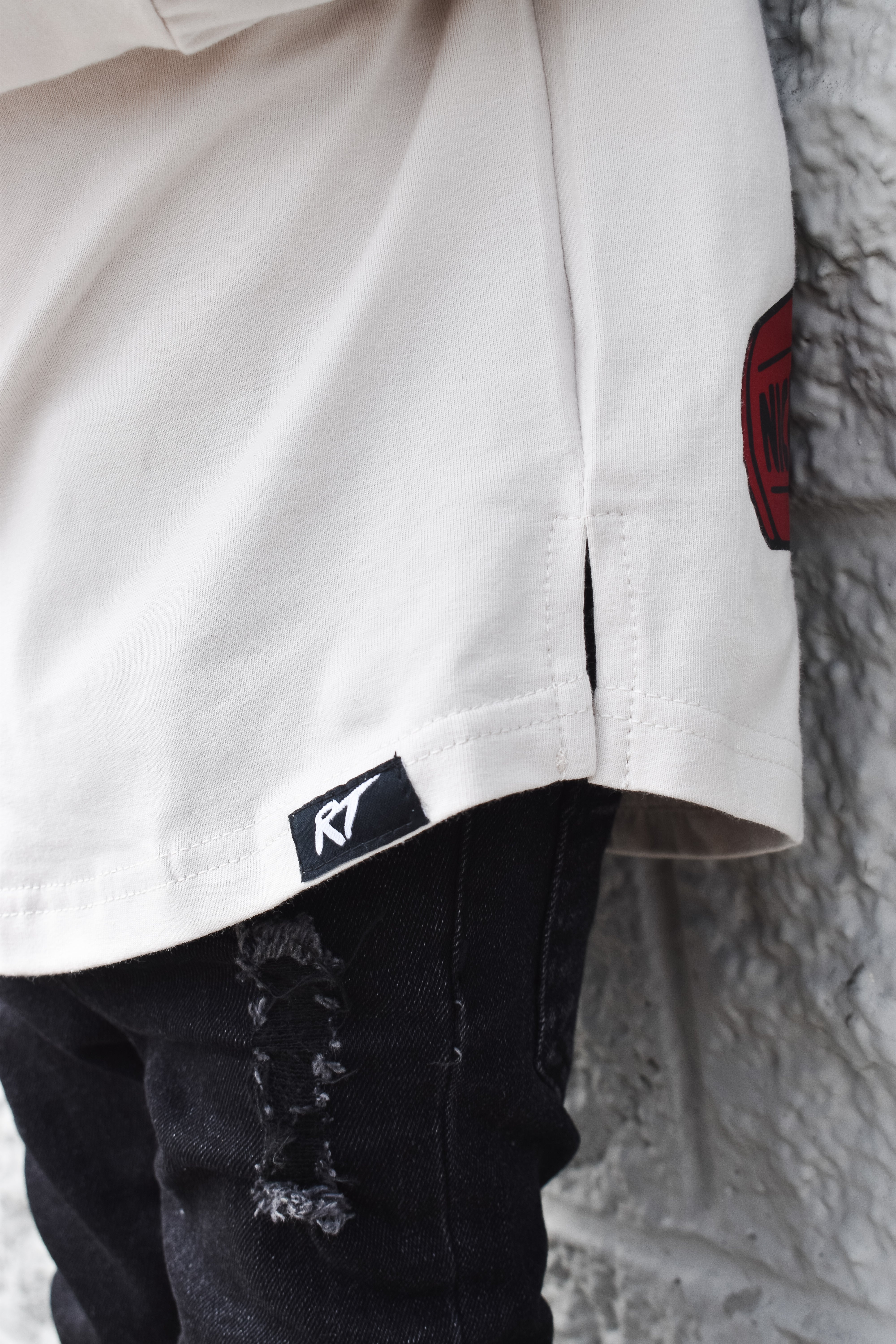 Close-up of a white shirt with a red logo and black pants against a textured wall.