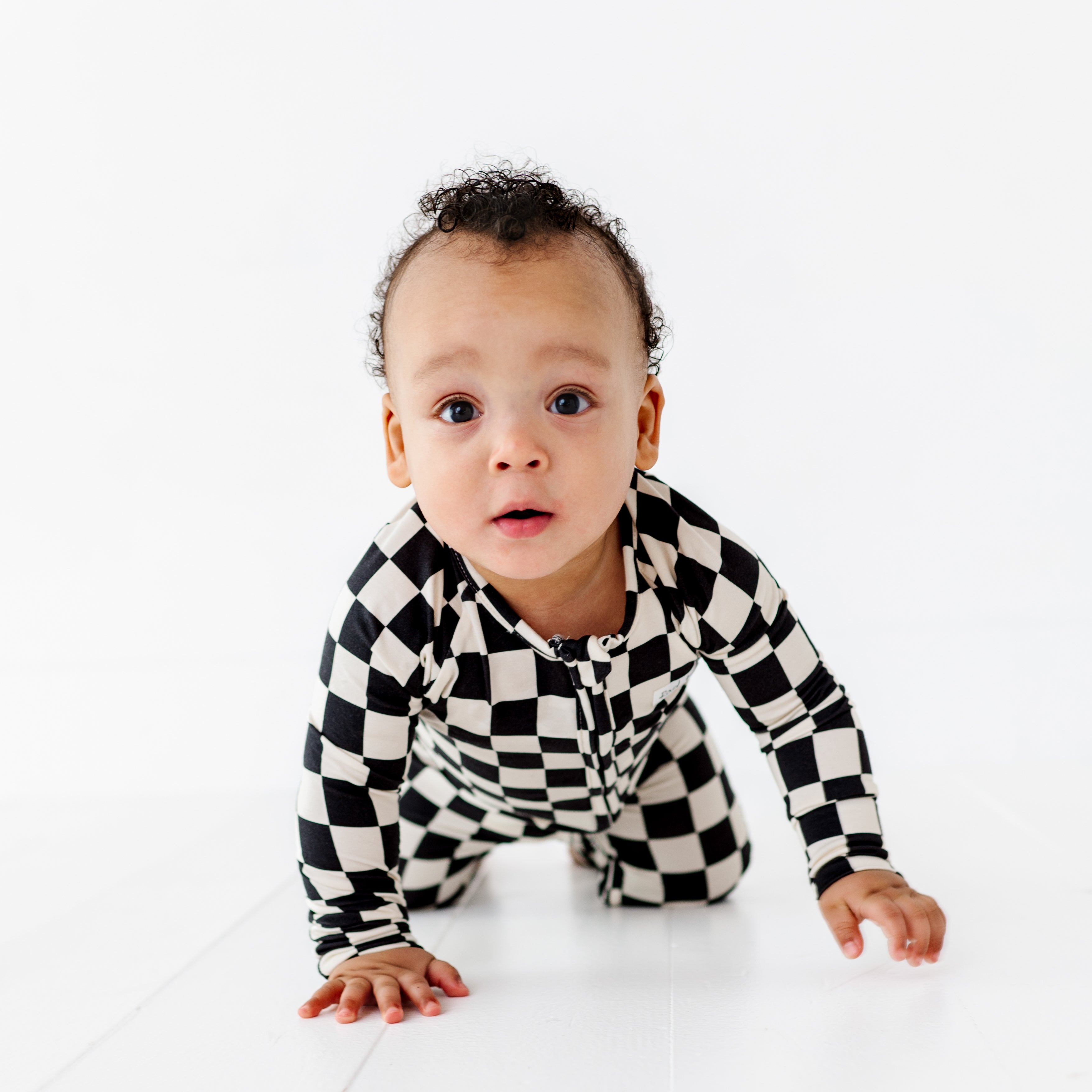 Toddler wearing black and white checkered bamboo onesie and crawling