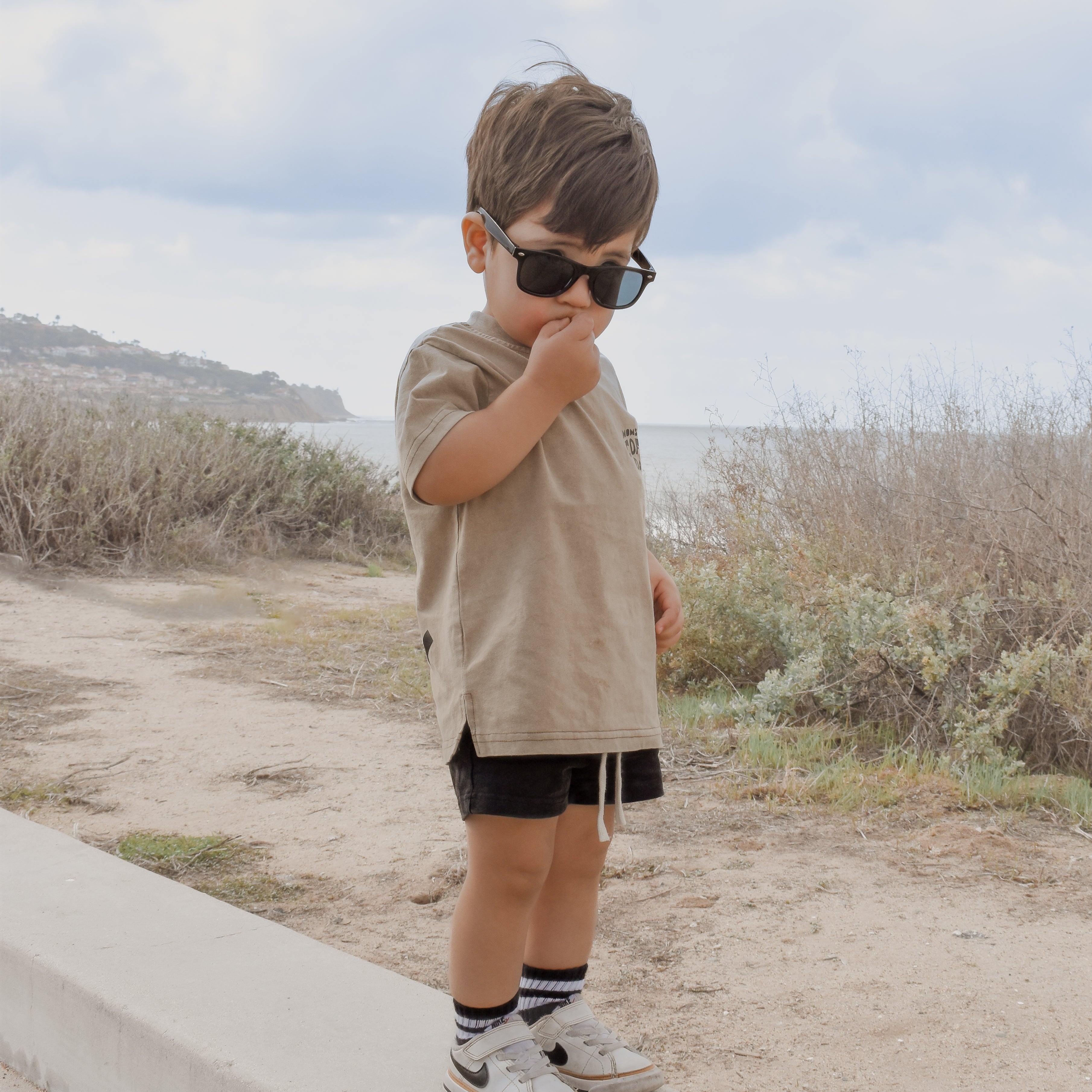 cute boy stands near a beach wearing moms coffee date t shirt featuring a perfect fit and durable materials