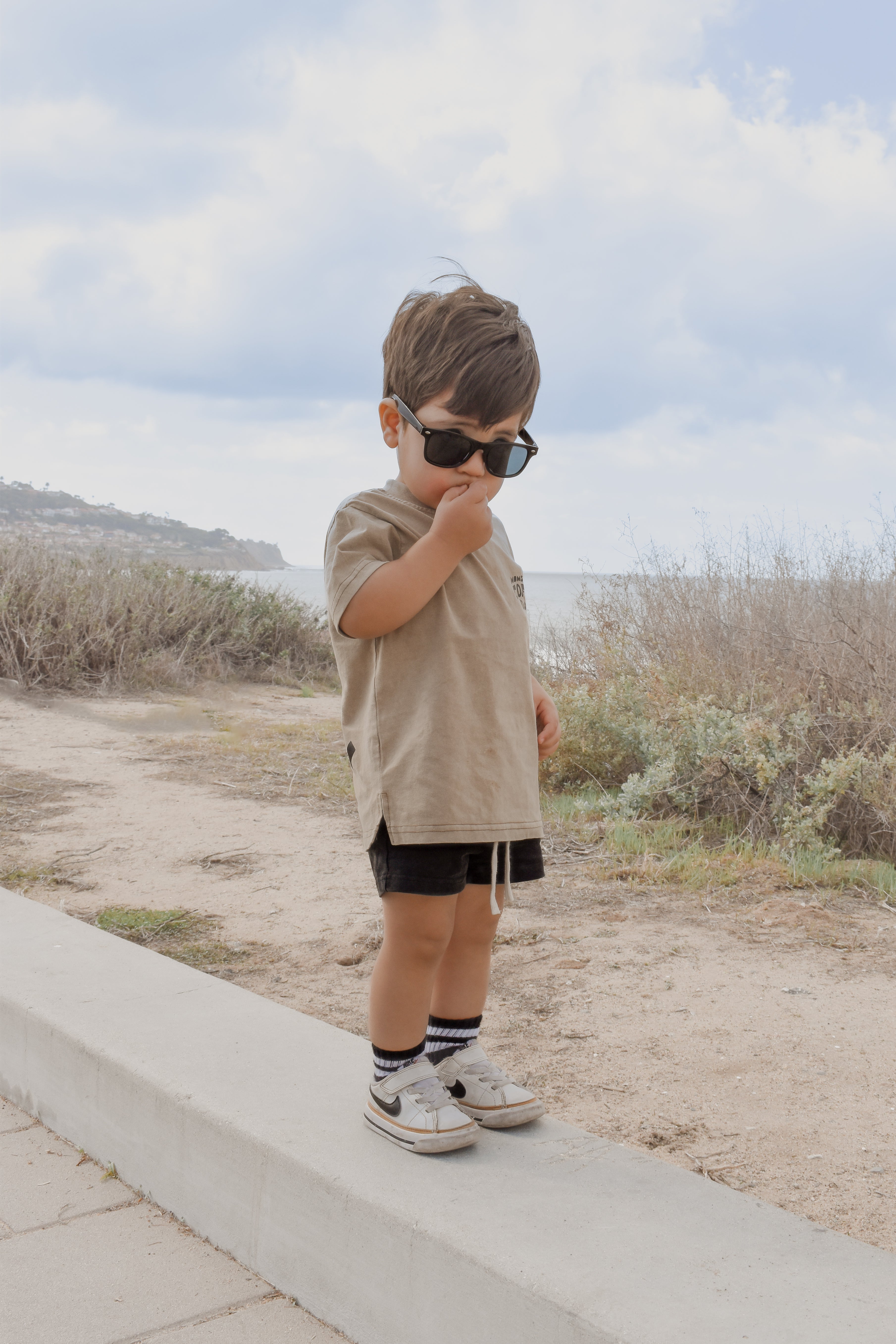 cute boy stands near a beach wearing moms coffee date t shirt featuring a perfect fit and durable materials